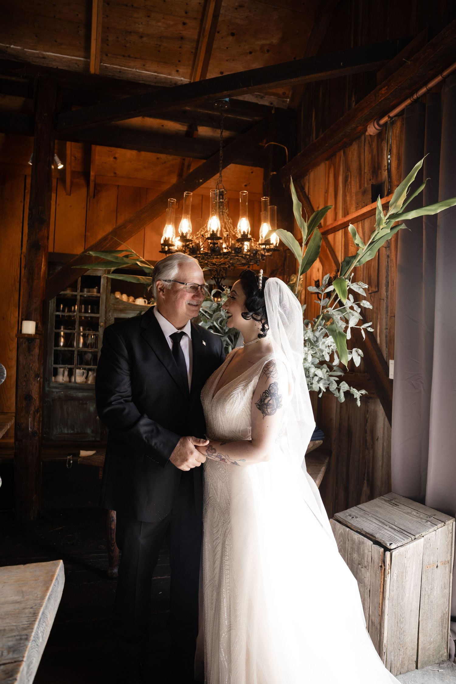 A couple shares an emotional moment in a barn with chandelier lighting and floral decorations.