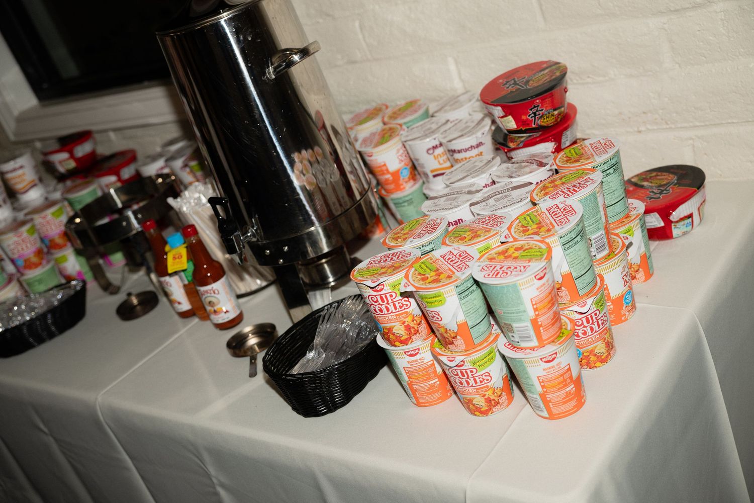 Table display with stacked Cup Noodles instant ramen cups and canned goods next to a beverage dispenser.
