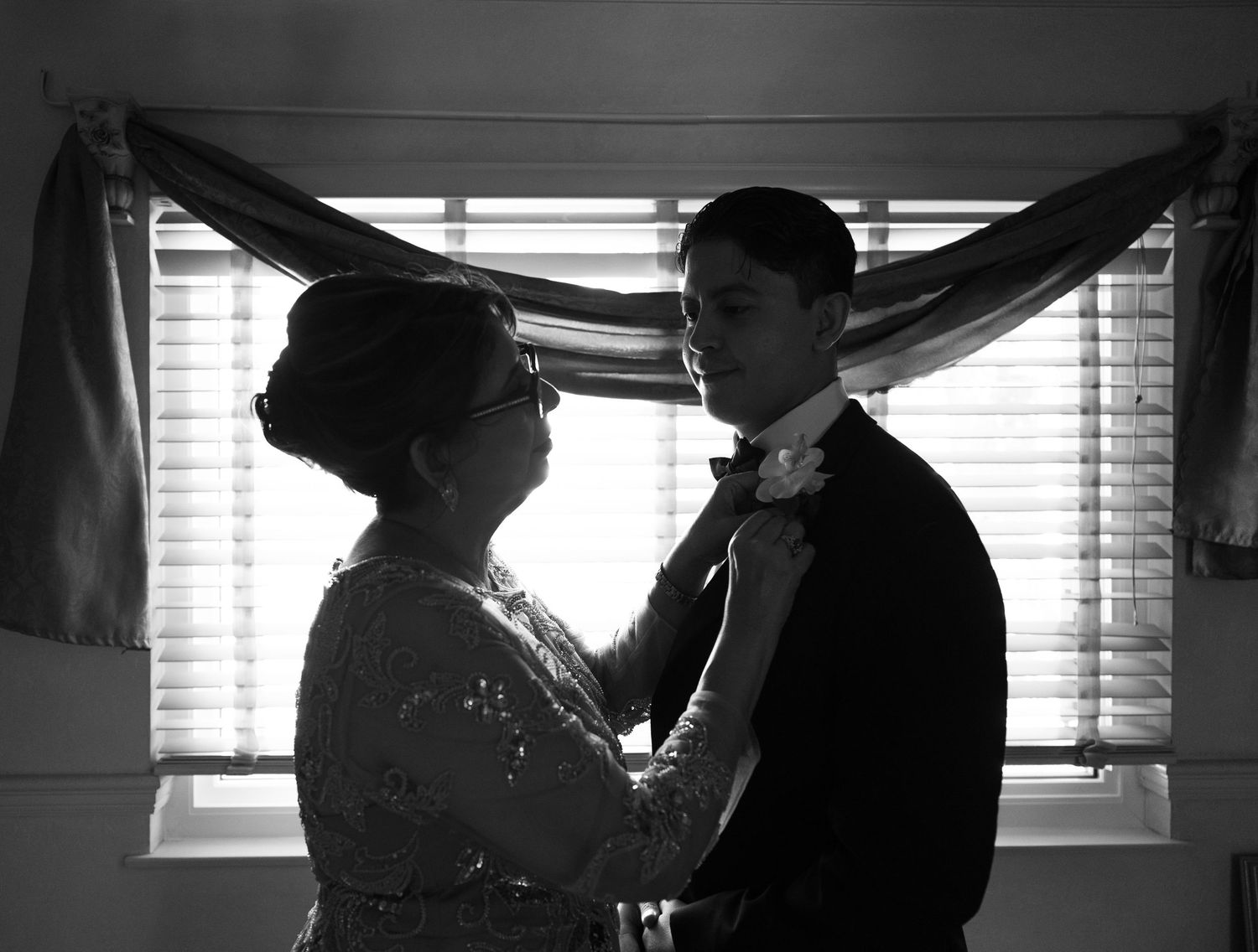Silhouetted figures in formal wear stand near a window in dramatic lighting.