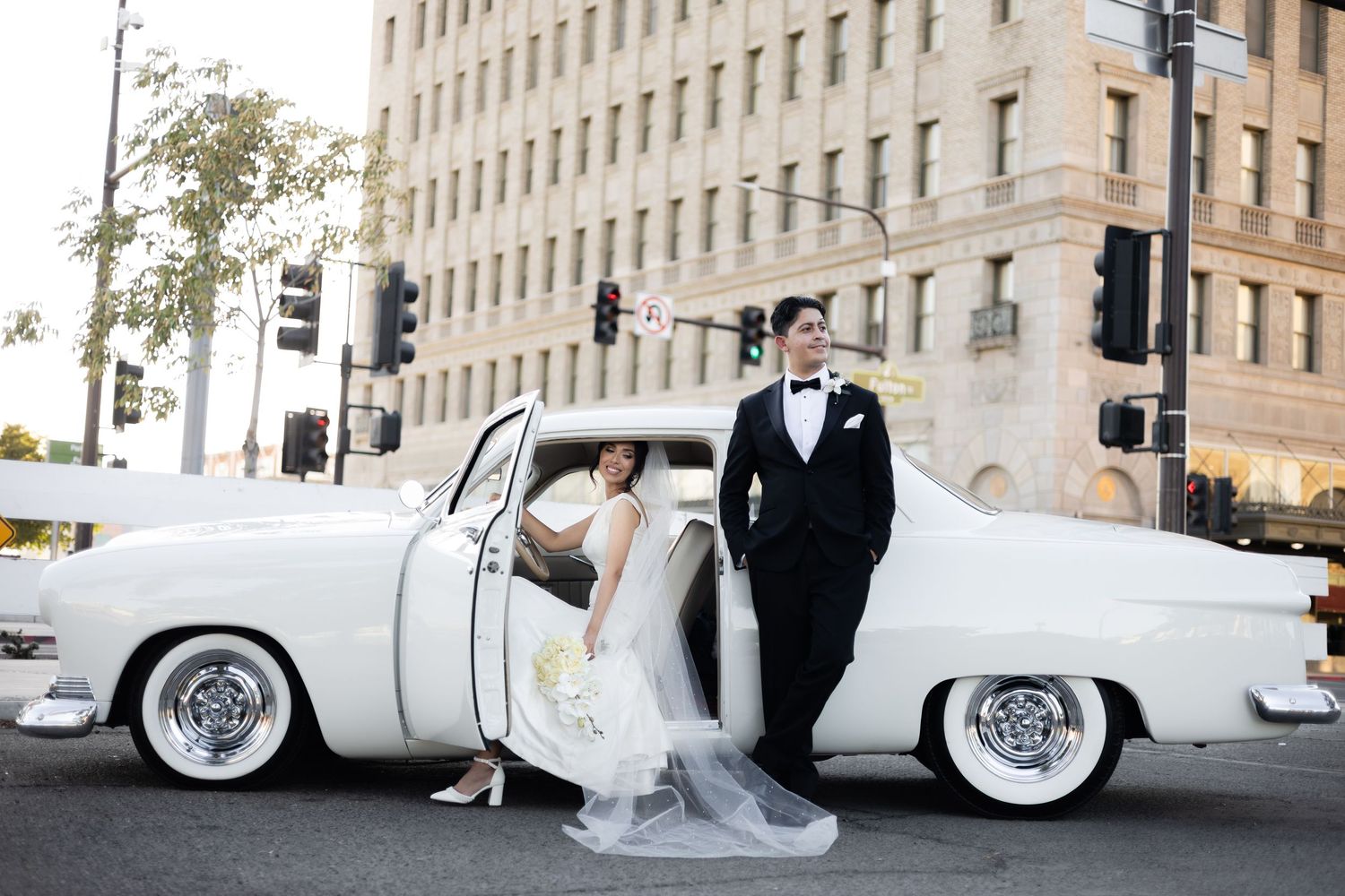 Wedding photography session featuring a classic white car and formal attire against city architecture.