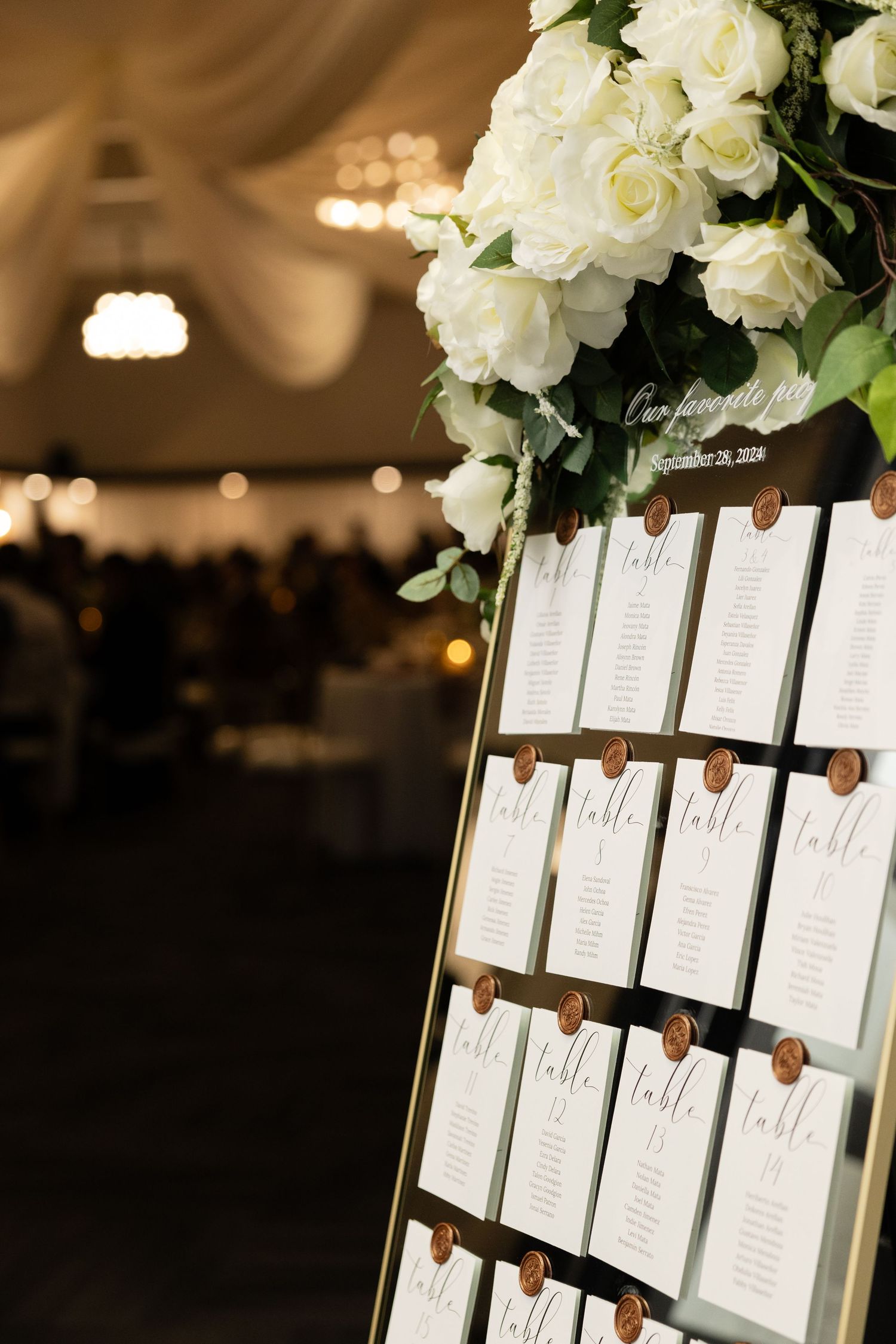 Elegant wedding seating chart display with white roses and printed name cards arranged on dark display boards.