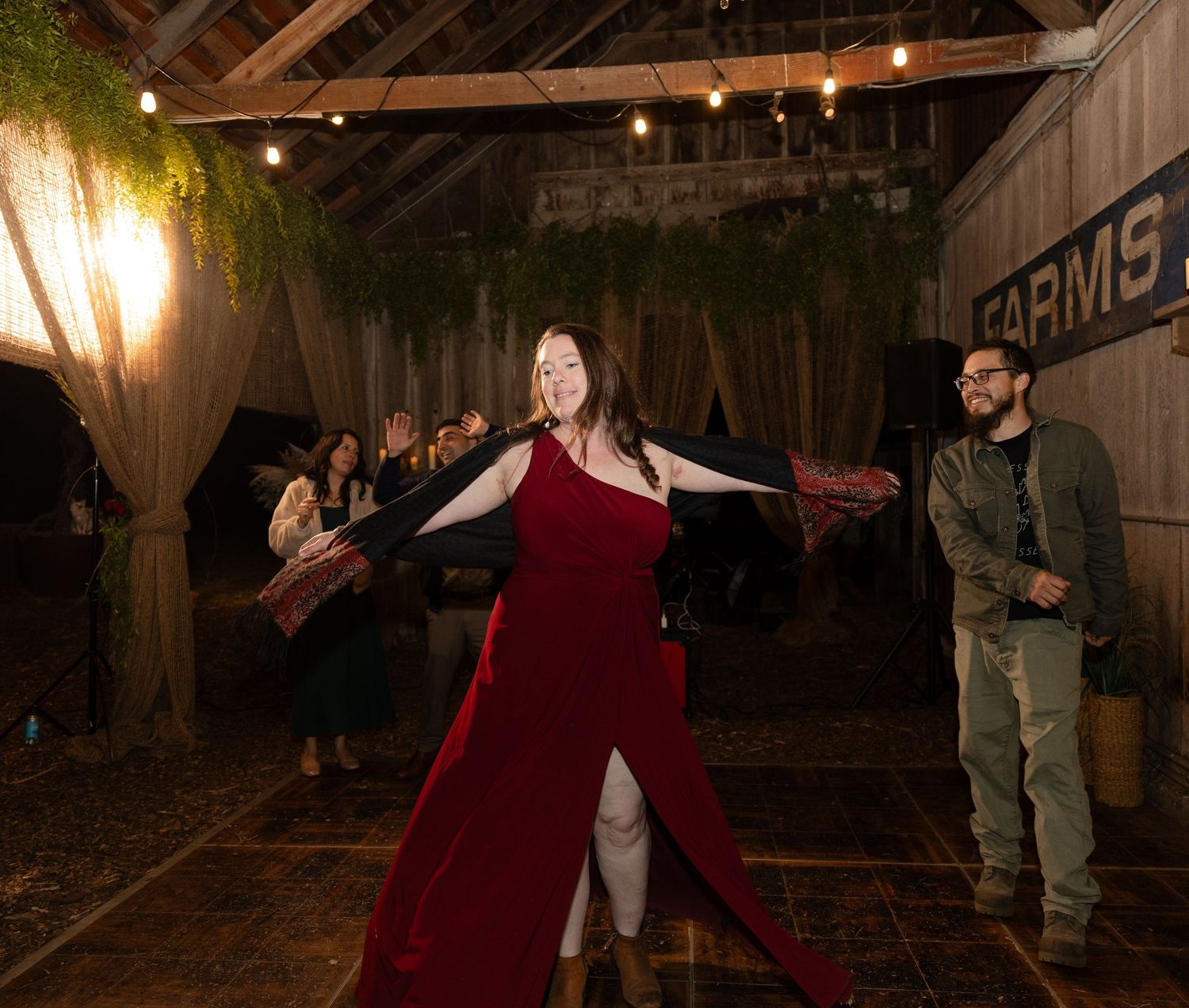 Couples dancing in a beautifully lit barn with wooden beams and greenery.