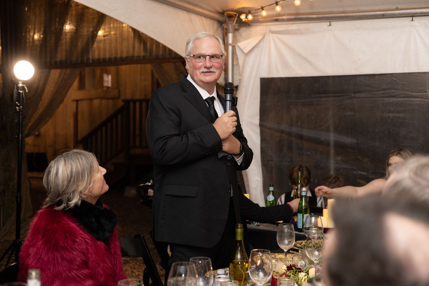 Indoor wedding reception with guests seated at tables under warm lighting.