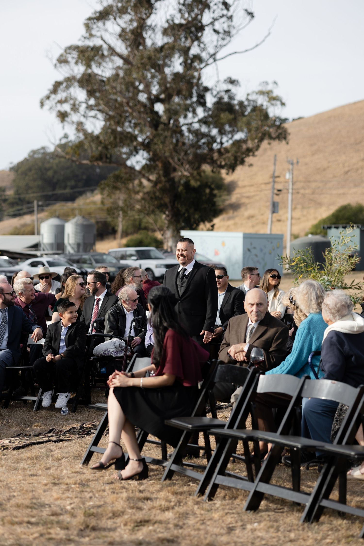 Panoramic view of outdoor wedding ceremony with guests seated against rolling hills.