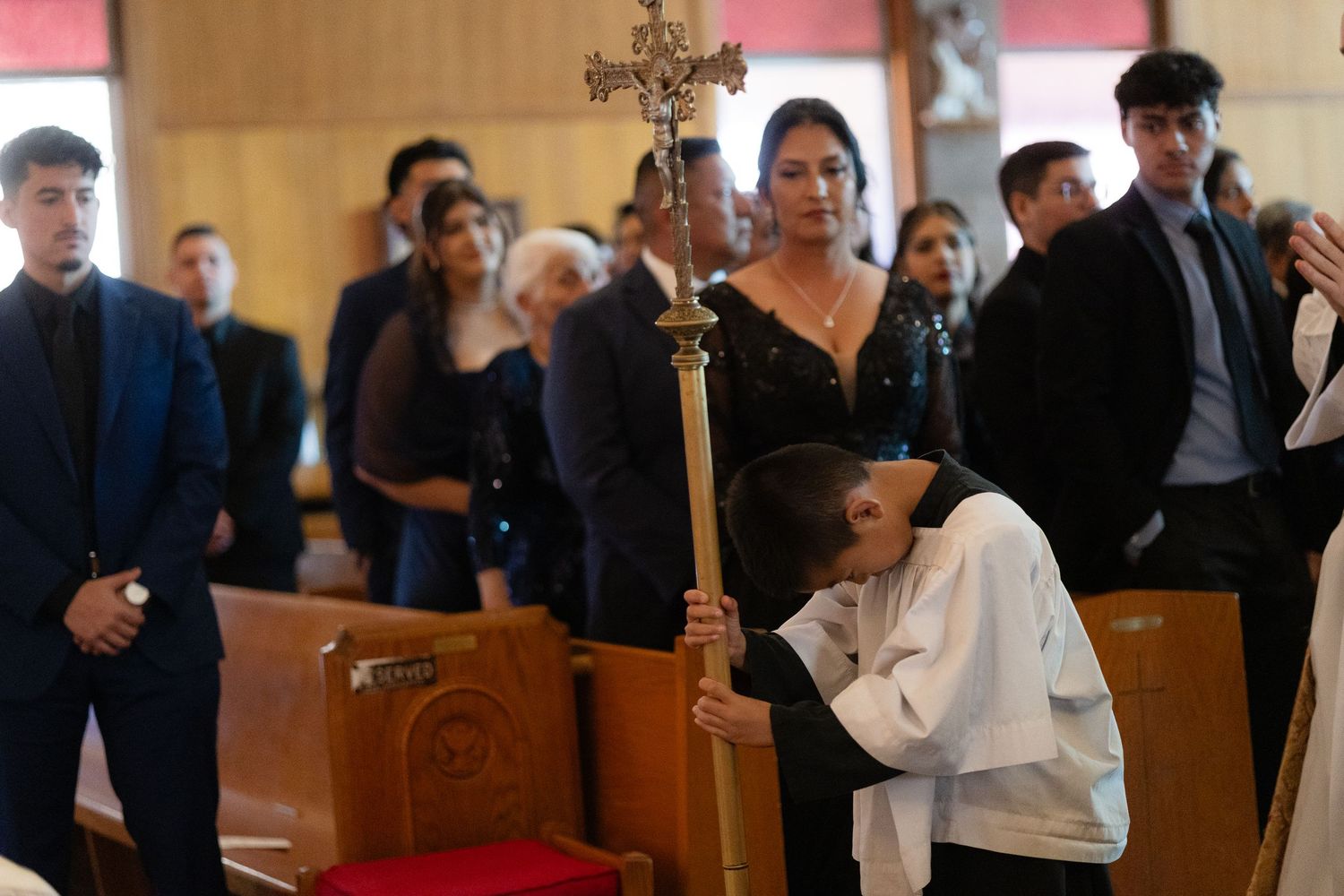 Church ceremony with attendees gathered while someone holds a ceremonial cross.