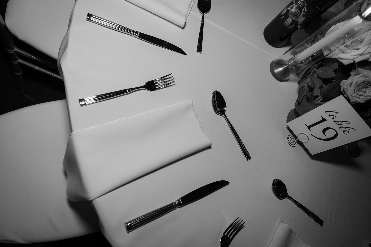 Black and white photo of place settings with silverware arranged on white tablecloths.