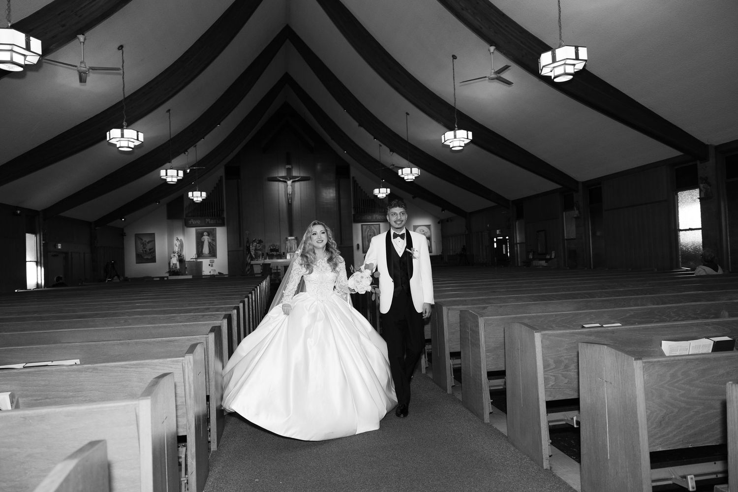 Black and white photo of couple walking down church aisle in traditional wedding attire.