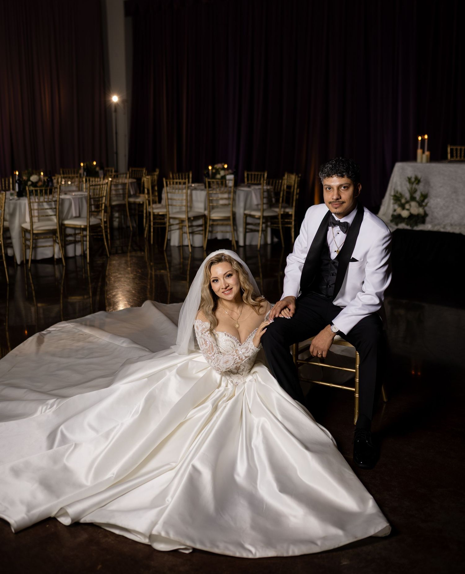 An elegant wedding photo in a dimly lit reception venue with gold chiavari chairs.