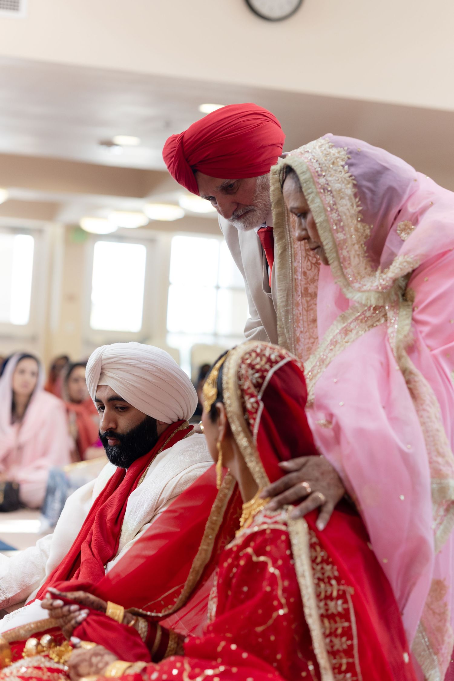 Sikh wedding ceremony participants wearing traditional red and pink attire seated during religious proceedings.