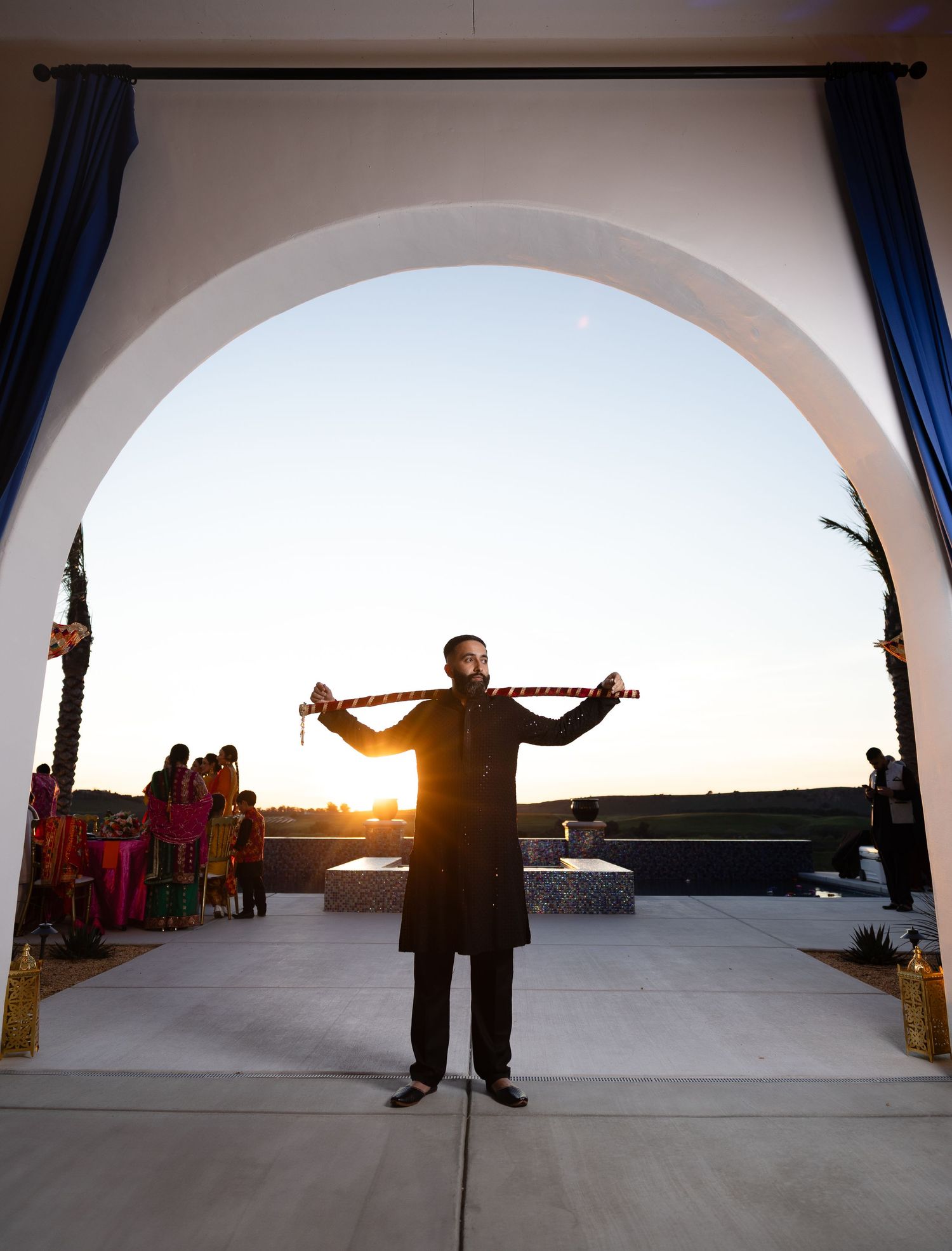 Silhouette of people dancing under arched columns at sunset.