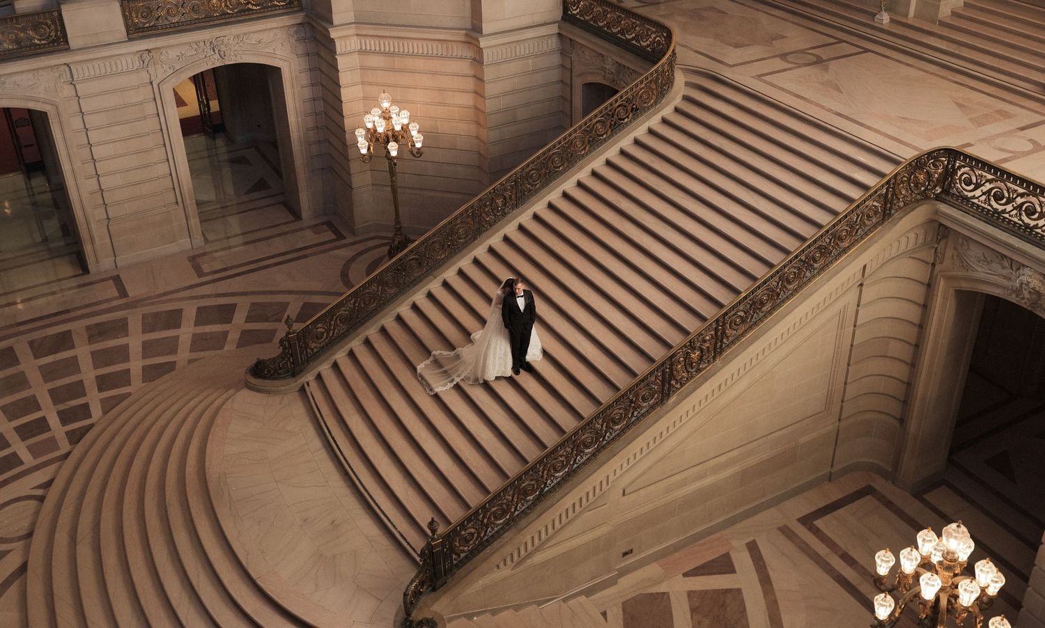 Elegant marble staircase with ornate railings and crystal chandeliers in a grand historic building interior.