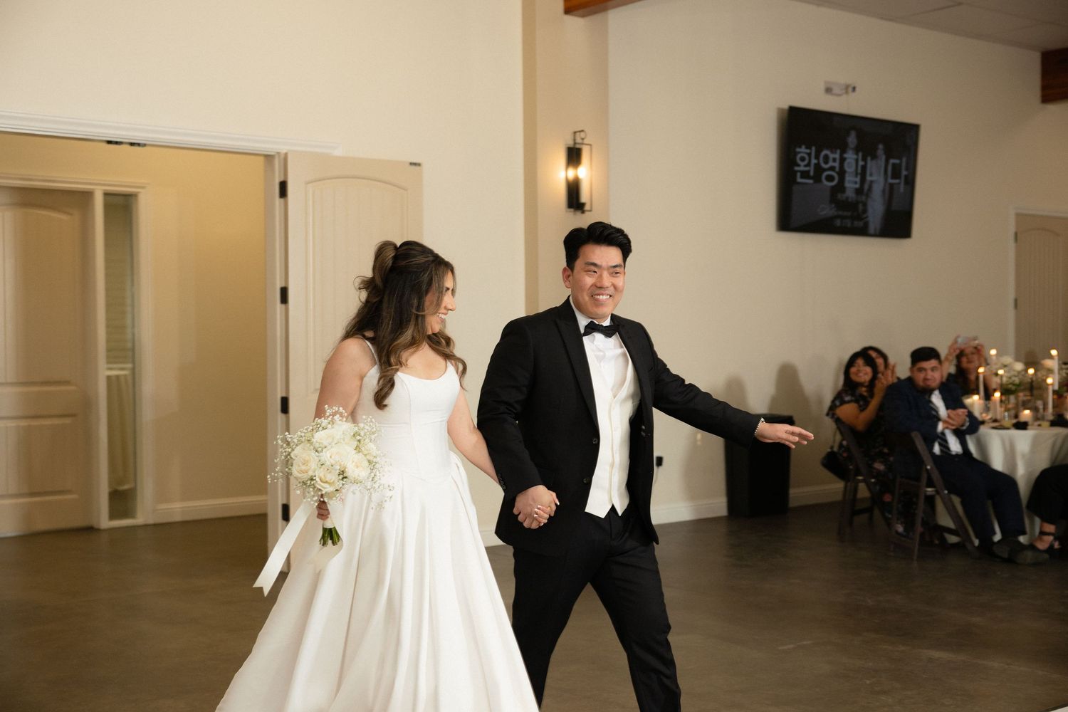 Bride and groom making grand entrance at wedding reception in elegant white venue.