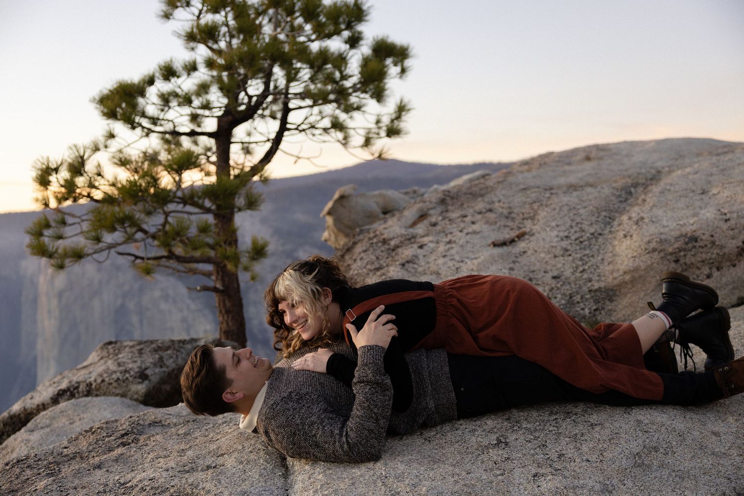 A couple lies together on rocky ground with mountain views in the background.