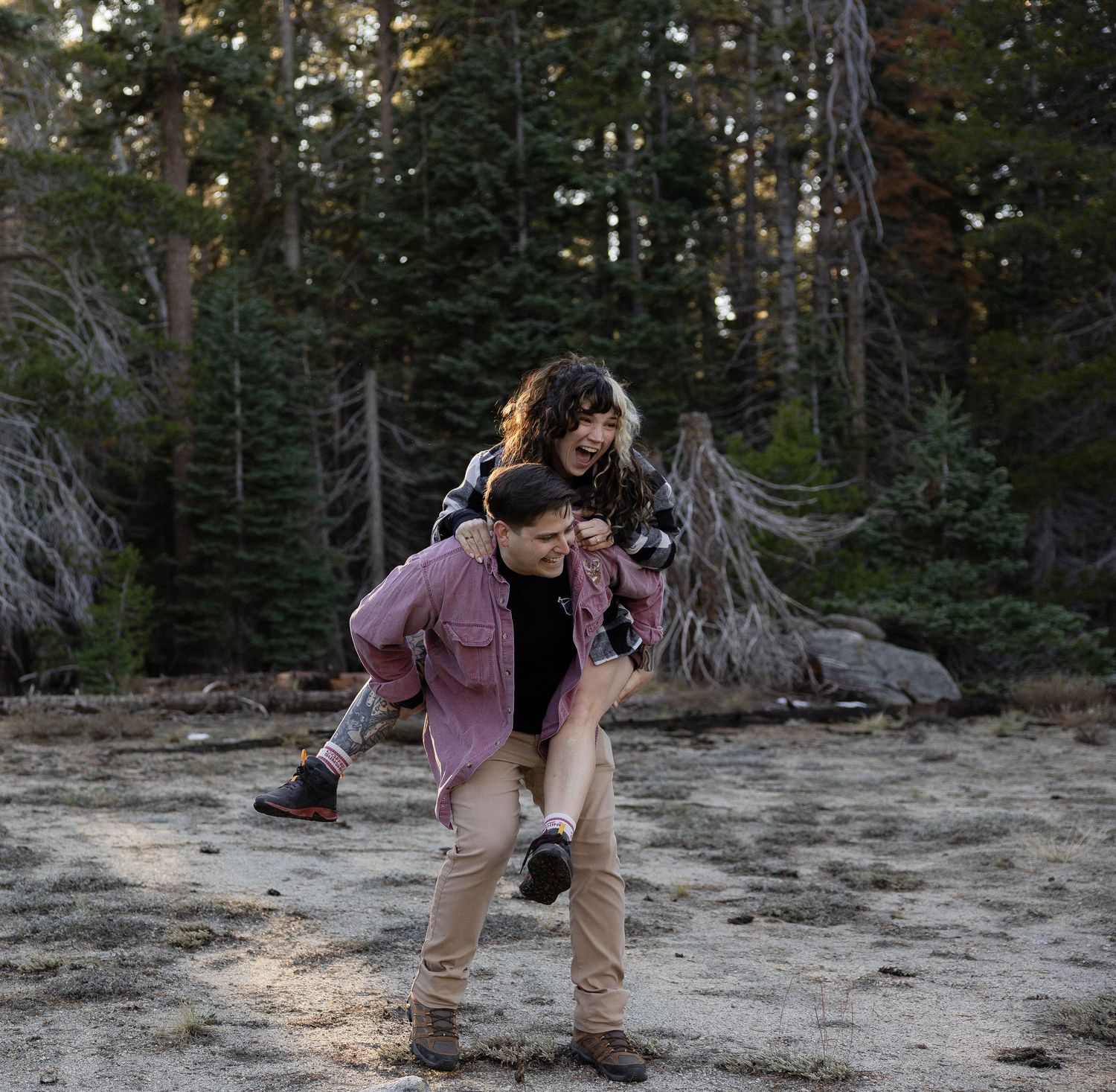Couple playfully posing on rocky ground surrounded by pine trees.