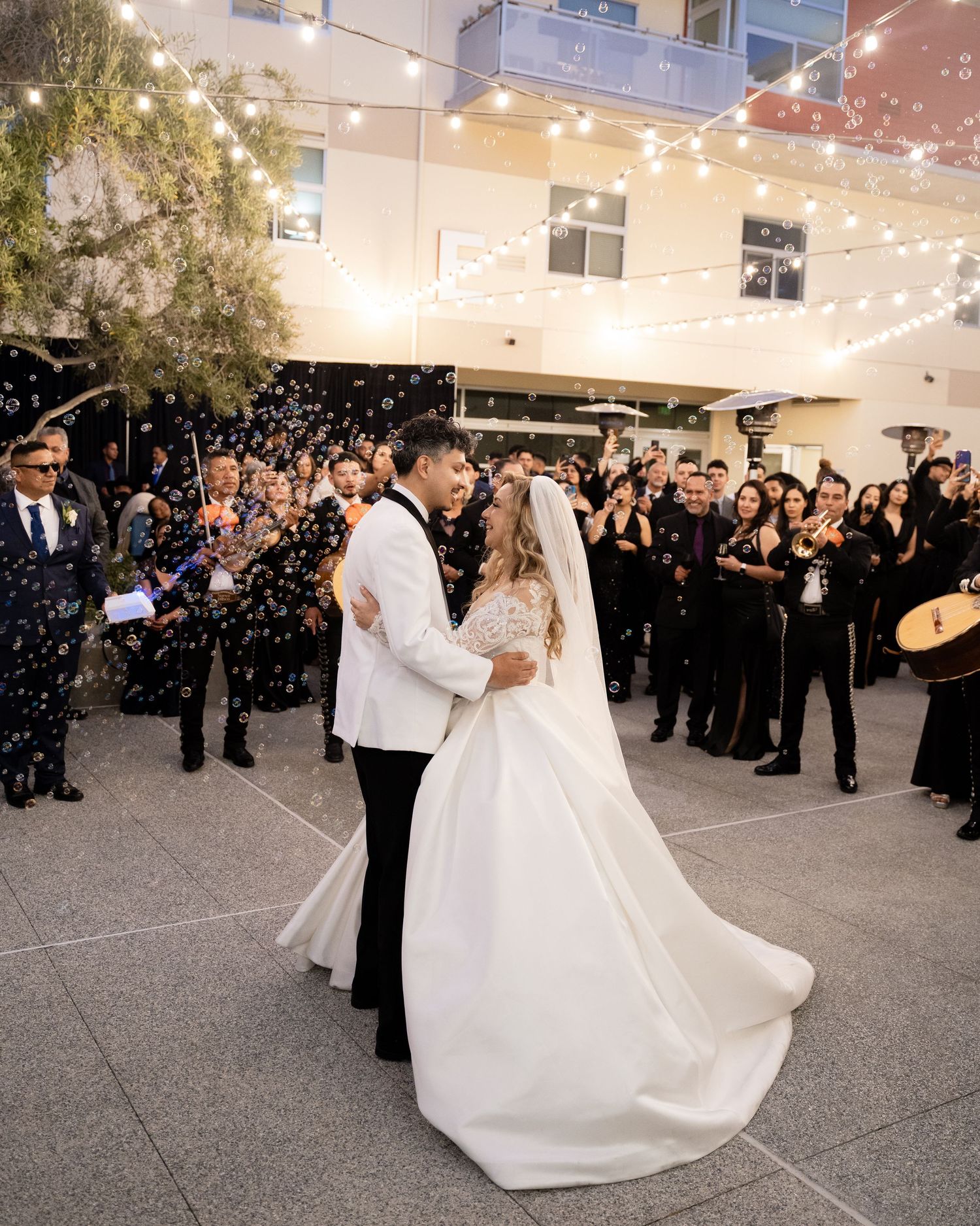 Wedding couple performs their first dance surrounded by guests in an outdoor reception space.