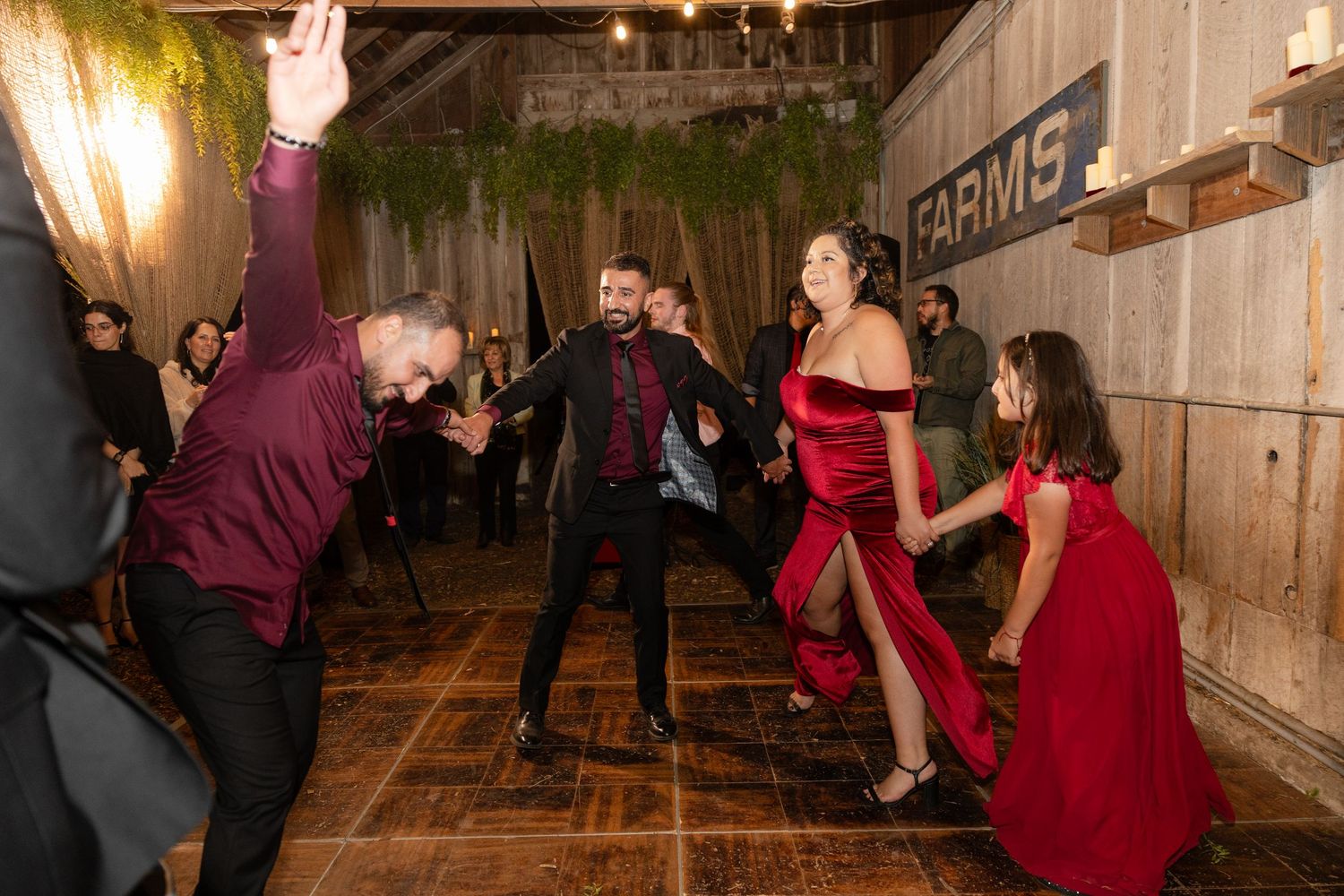 Couples dancing together at a barn reception with decorative greenery and string lights.