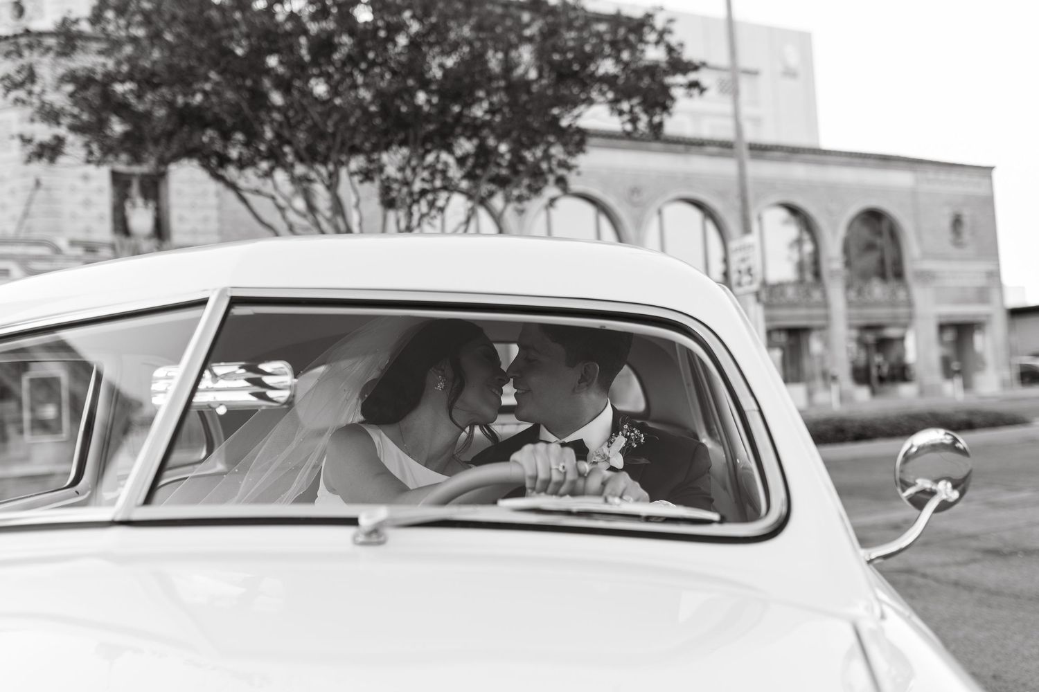 Vintage white car parked in front of a historic building on a sunny day.
