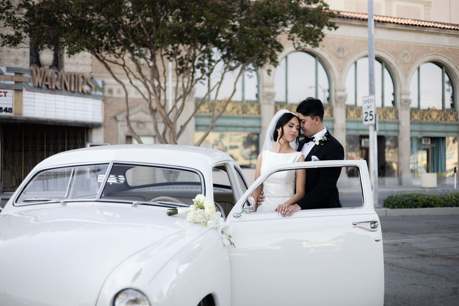 Vintage white car parked under trees for wedding photoshoot on urban street.