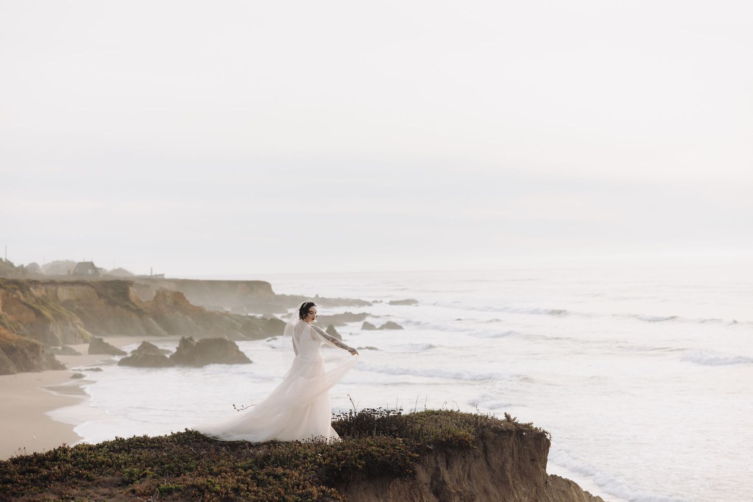 Ethereal wedding dress flowing in the wind on coastal cliffs overlooking dramatic ocean views.