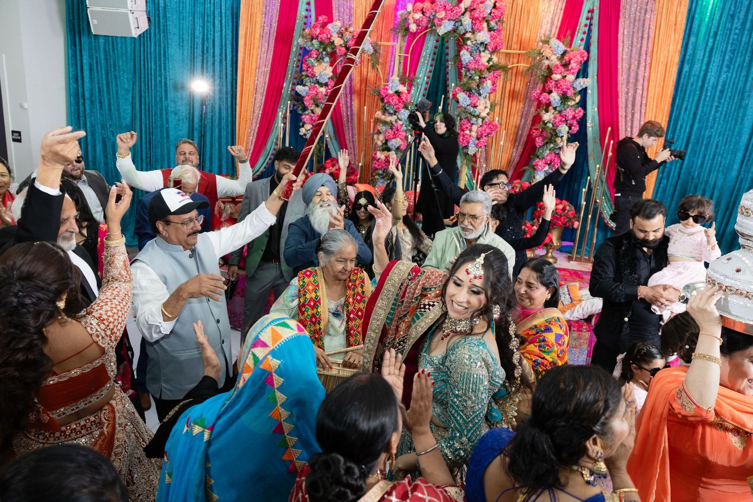 Colorful wedding reception venue with turquoise drapes and pink decorations showing guests mingling during celebration.
