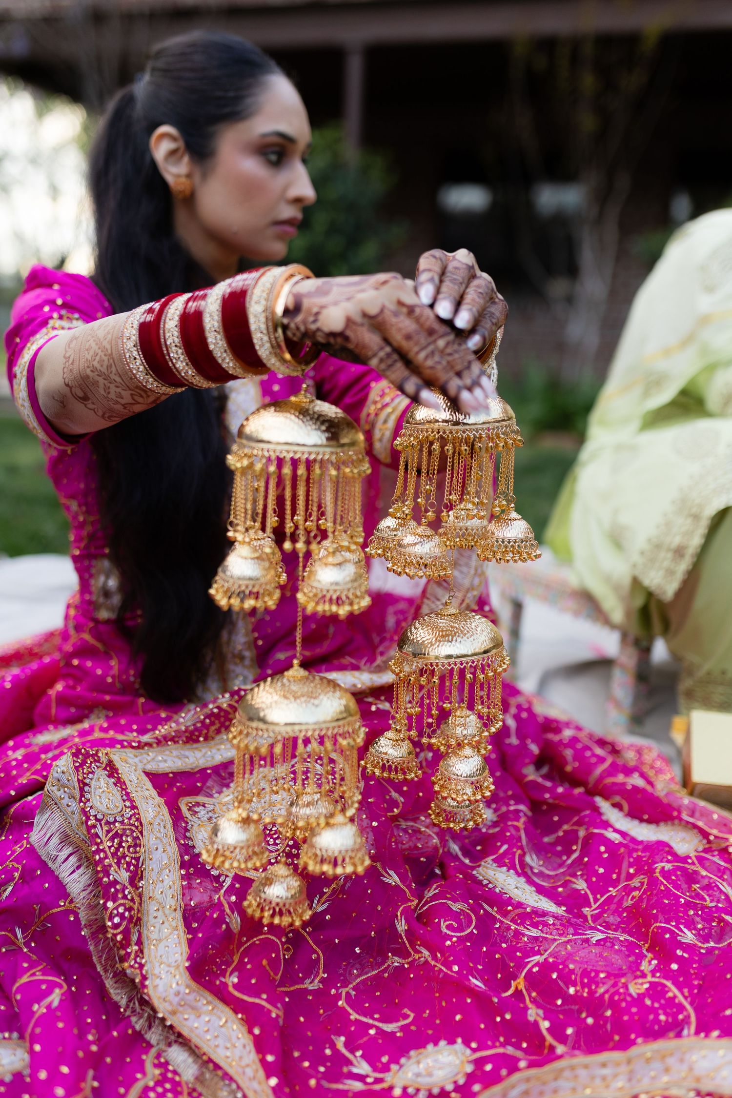 Traditional gold kalire wedding bangles displayed against bright pink embroidered fabric in natural light.
