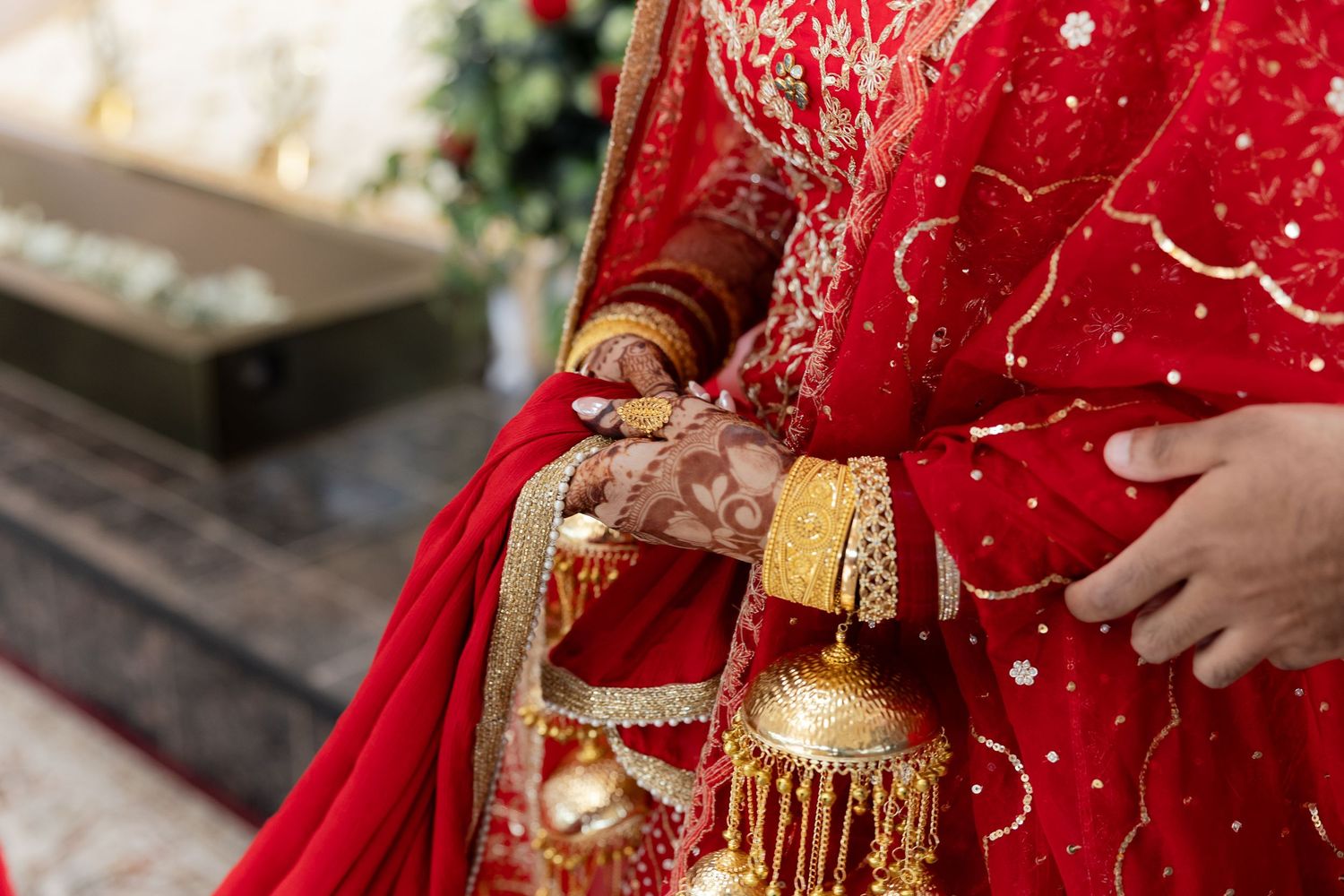 Close-up details of red and gold embroidered South Asian wedding attire with traditional jewelry.