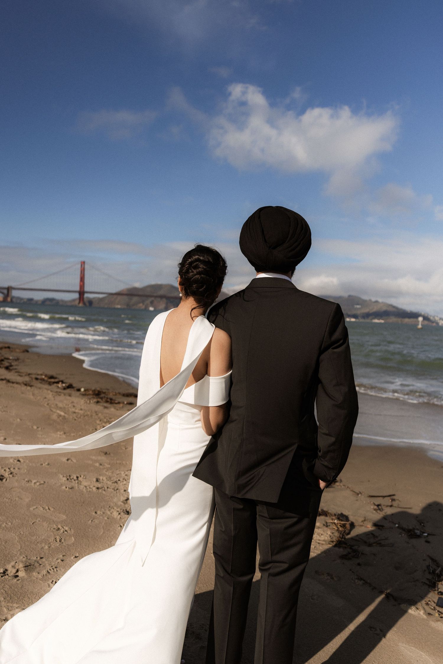 Wedding couple standing on Baker Beach with the iconic Golden Gate Bridge in the background.
