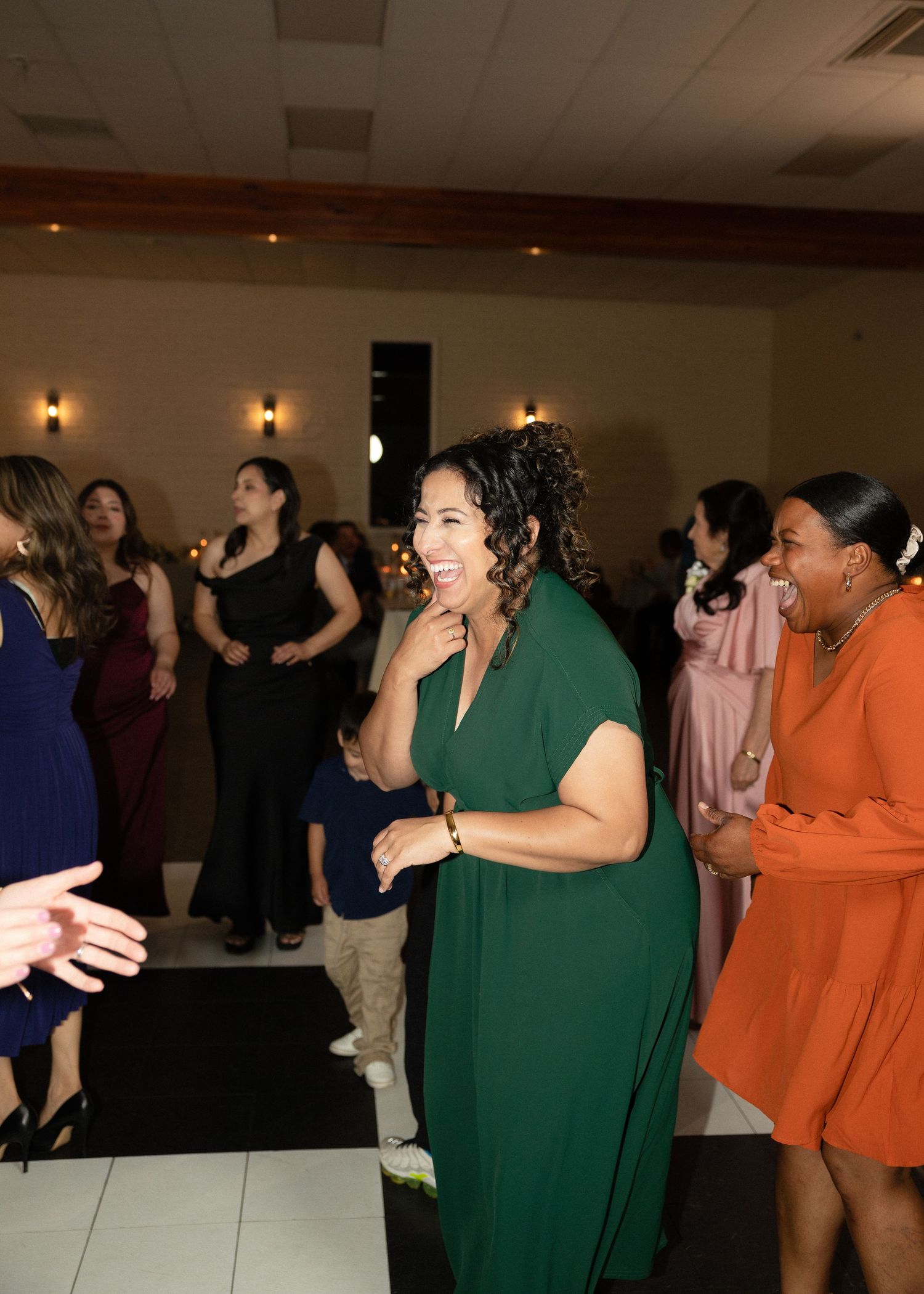 Woman in green dress smiling and dancing at an elegant wedding reception.