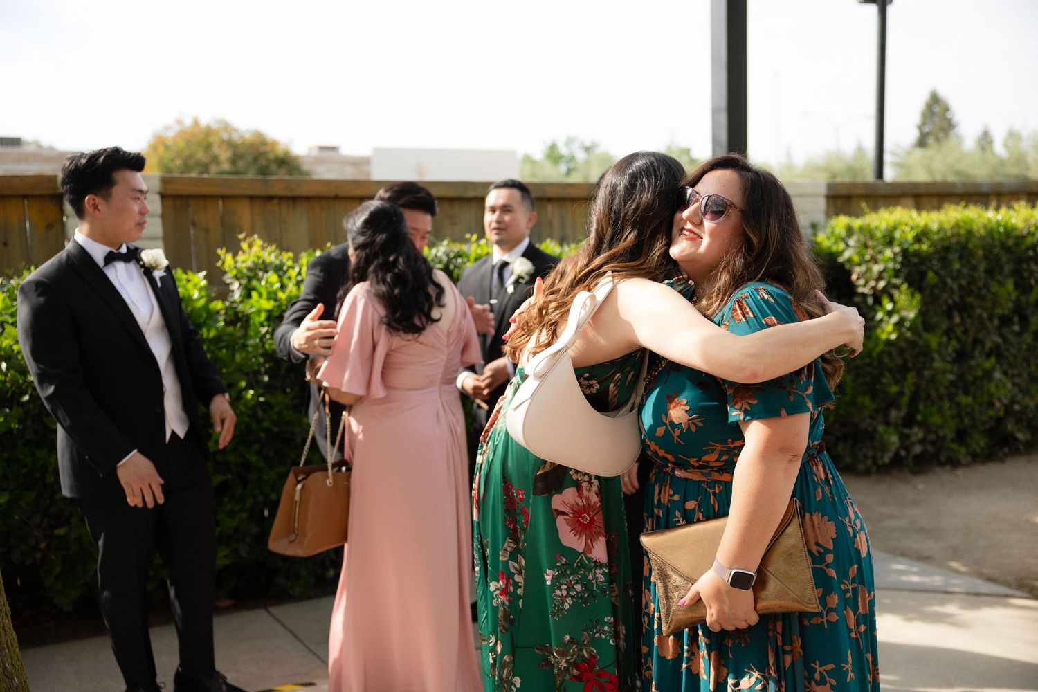 Wedding guests in formal attire greeting and embracing outside ceremony venue.