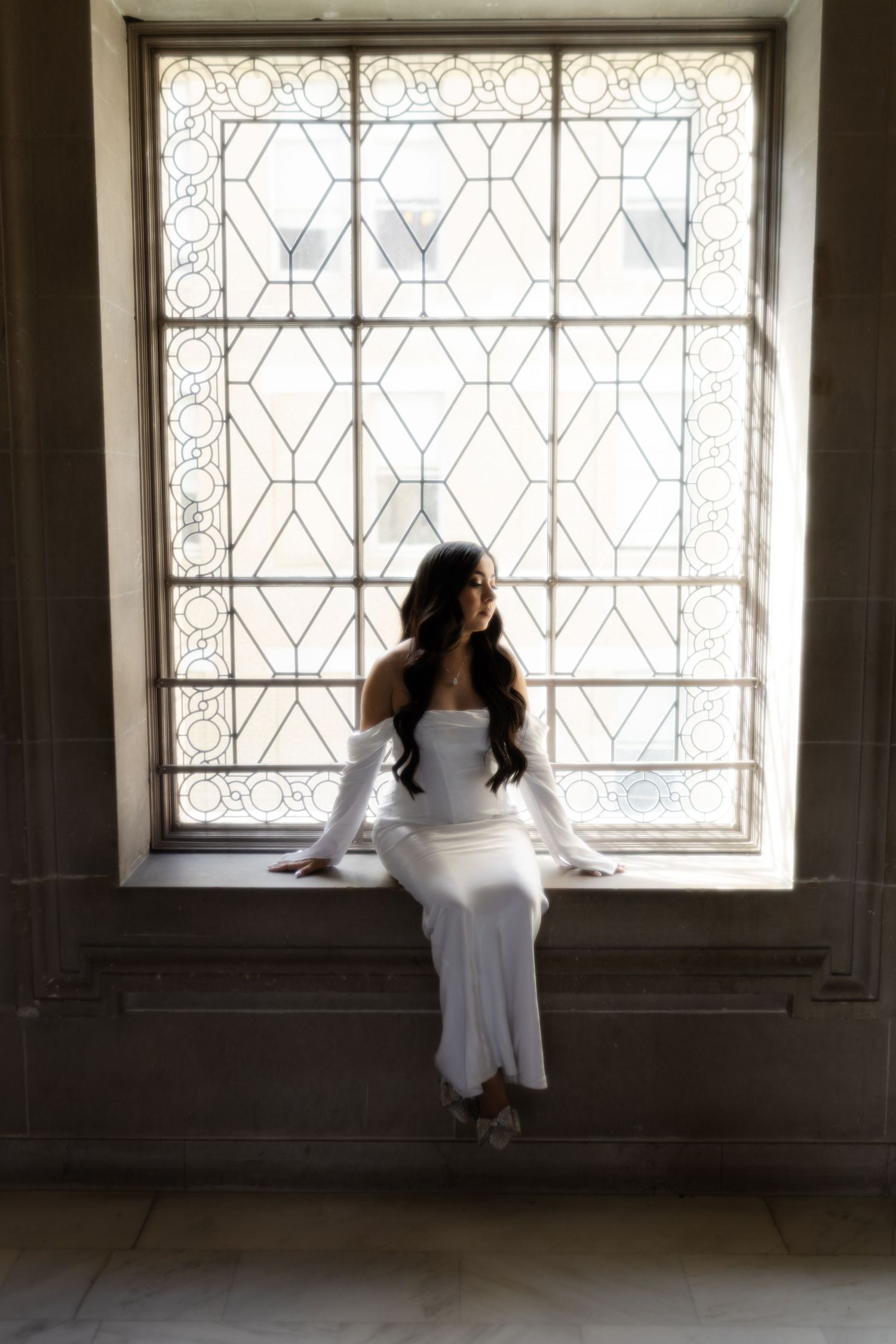 A figure in white sits contemplatively by a decorative window in a series of moody black and white photographs.