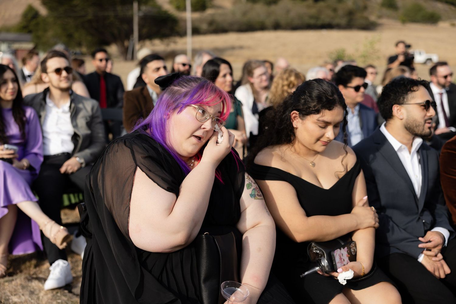 Wedding guests in formal attire watching ceremony in an outdoor desert setting.