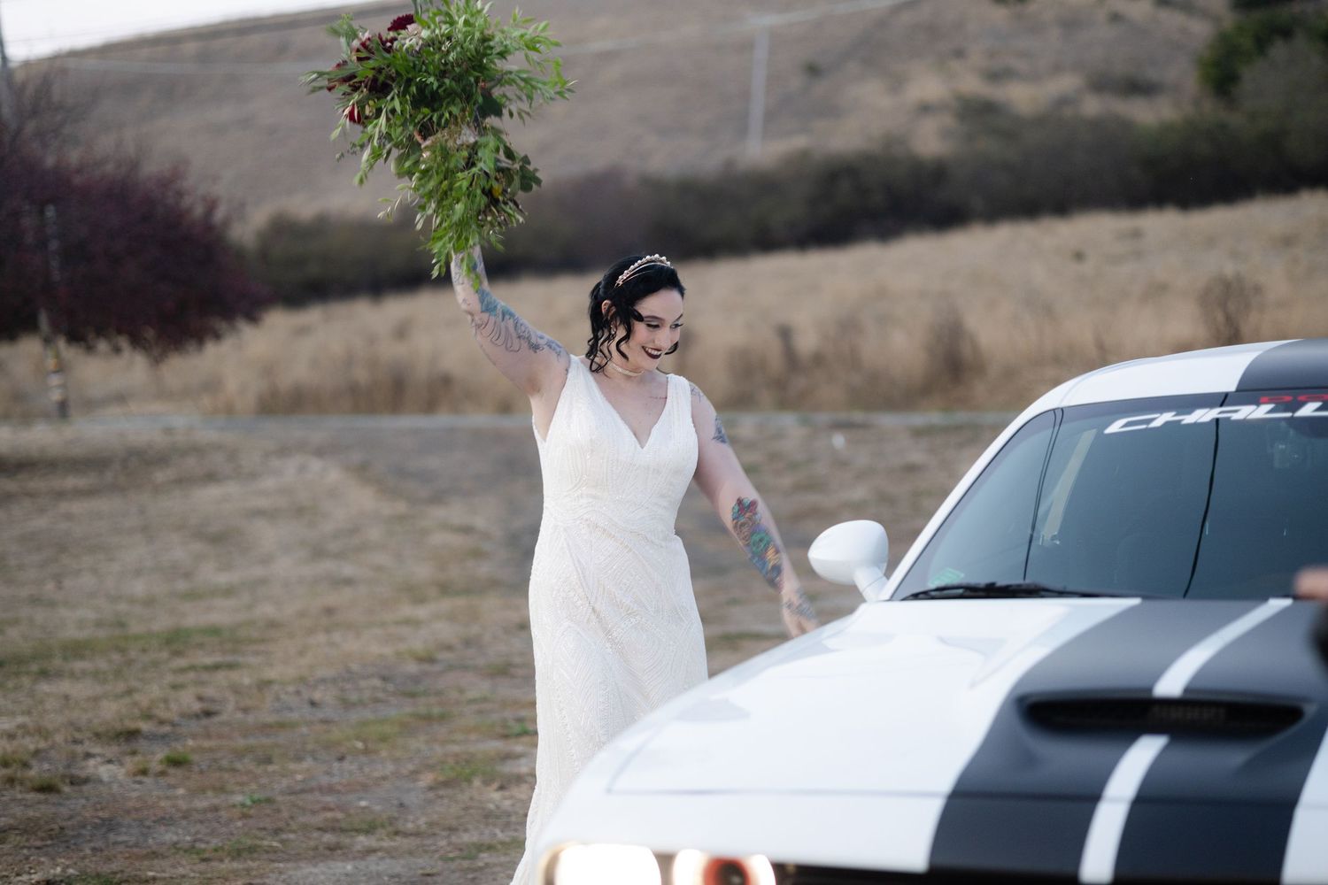 Wedding party members gather near parked cars at an outdoor venue.