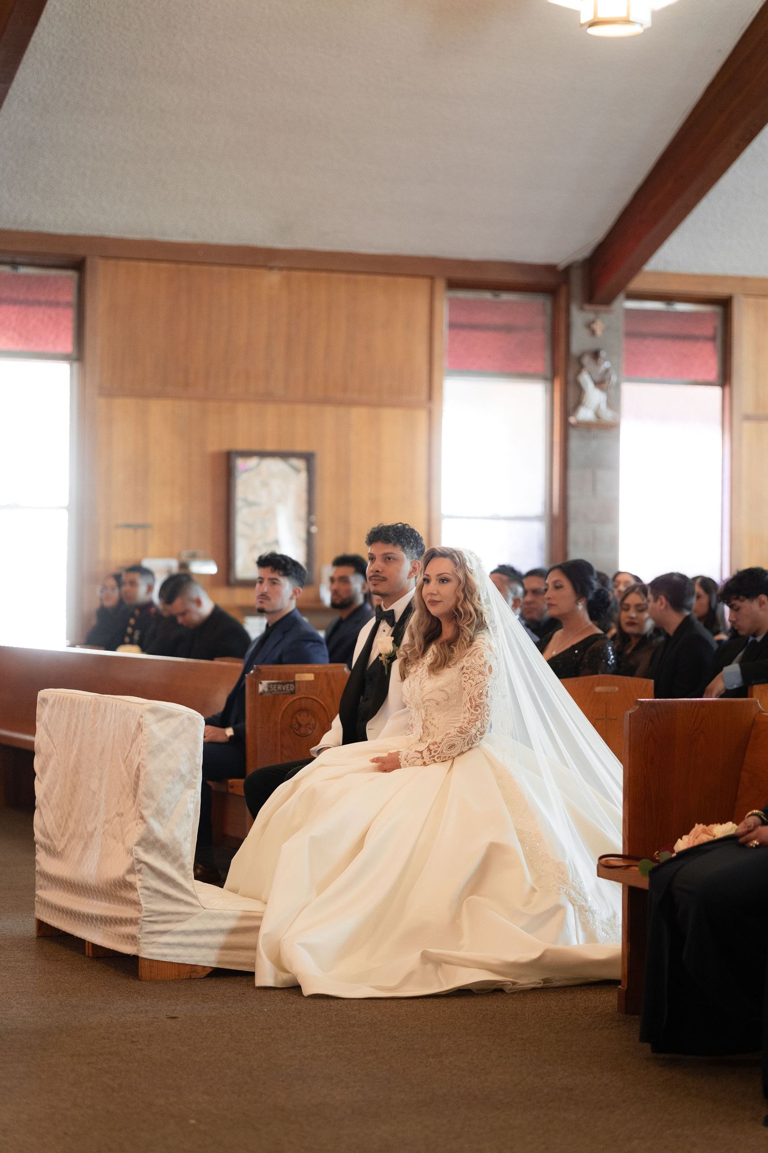 Wedding ceremony in a church with wooden pews and guests watching the proceedings.