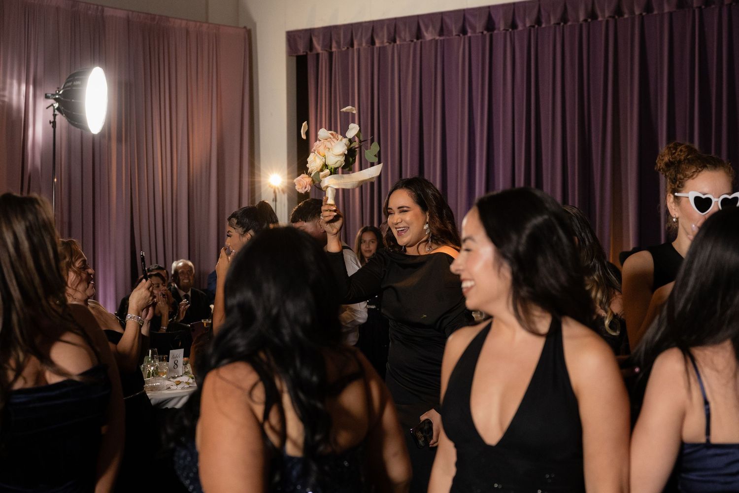 Wedding reception guests dancing and mingling in a venue with purple drapes.