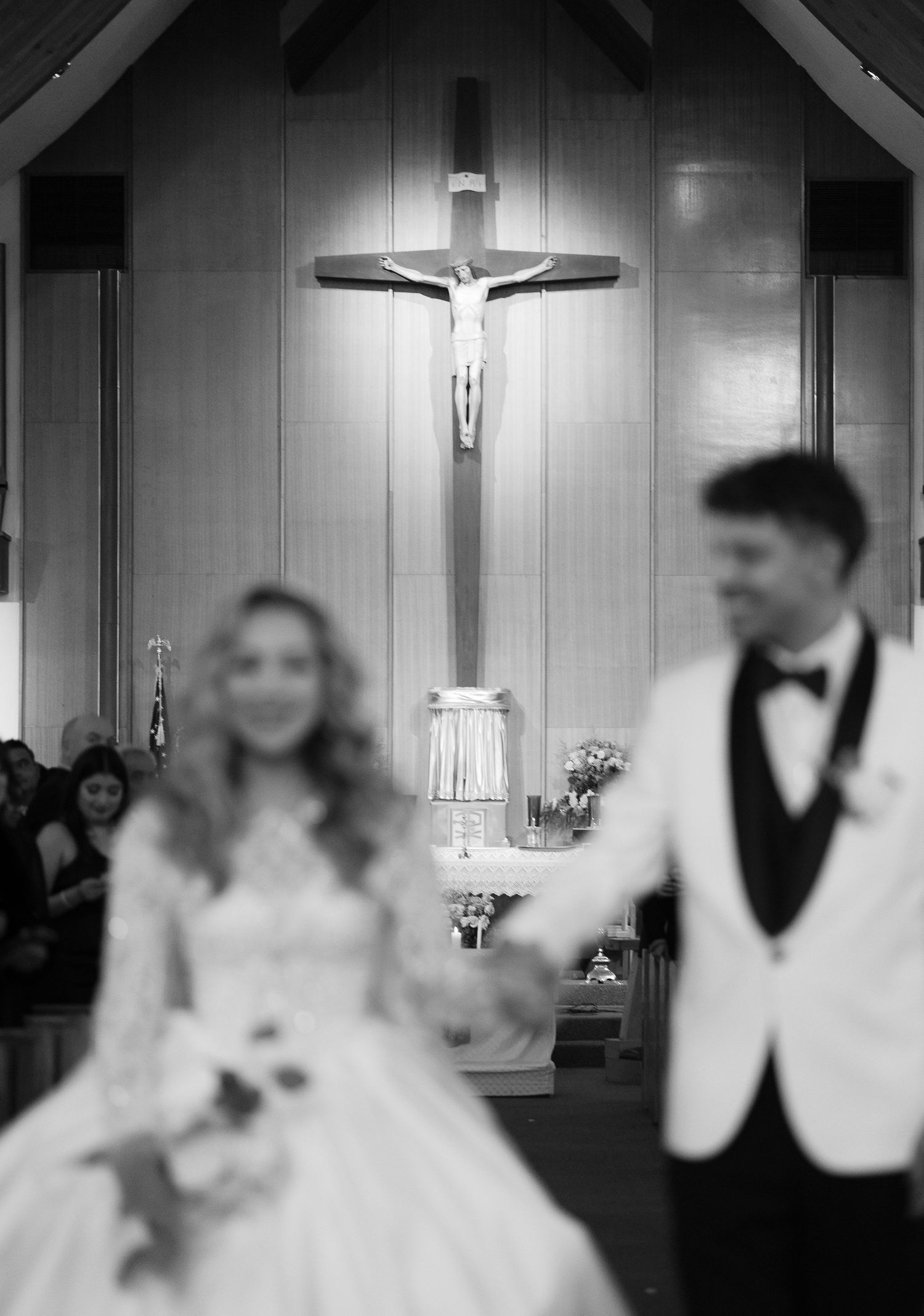 A black and white wedding photo with a prominent crucifix hanging above the altar.