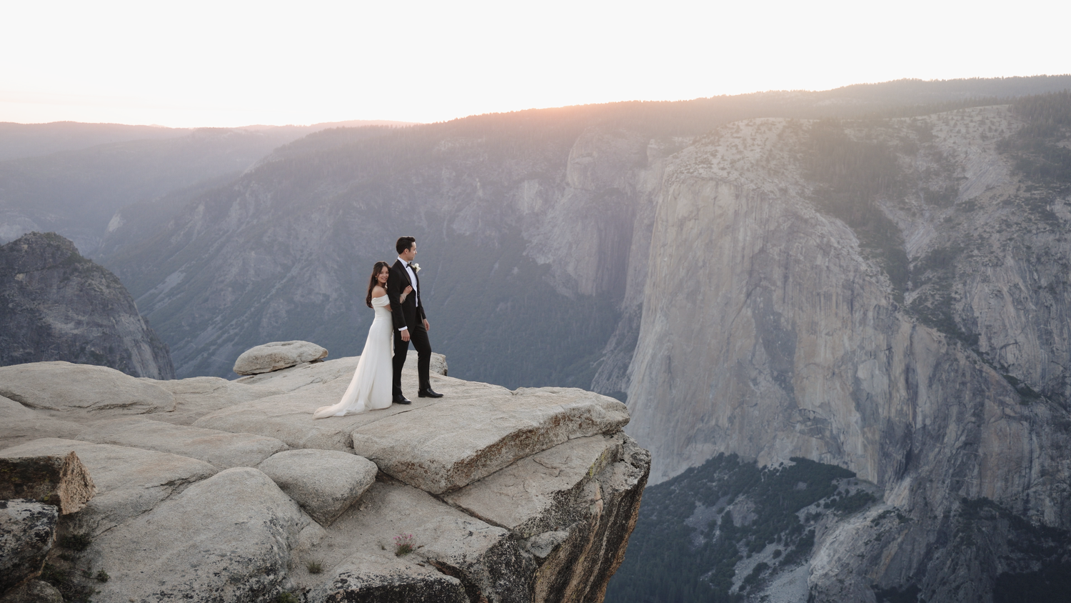 Silhouette of couple standing on cliff edge overlooking dramatic mountain valley.