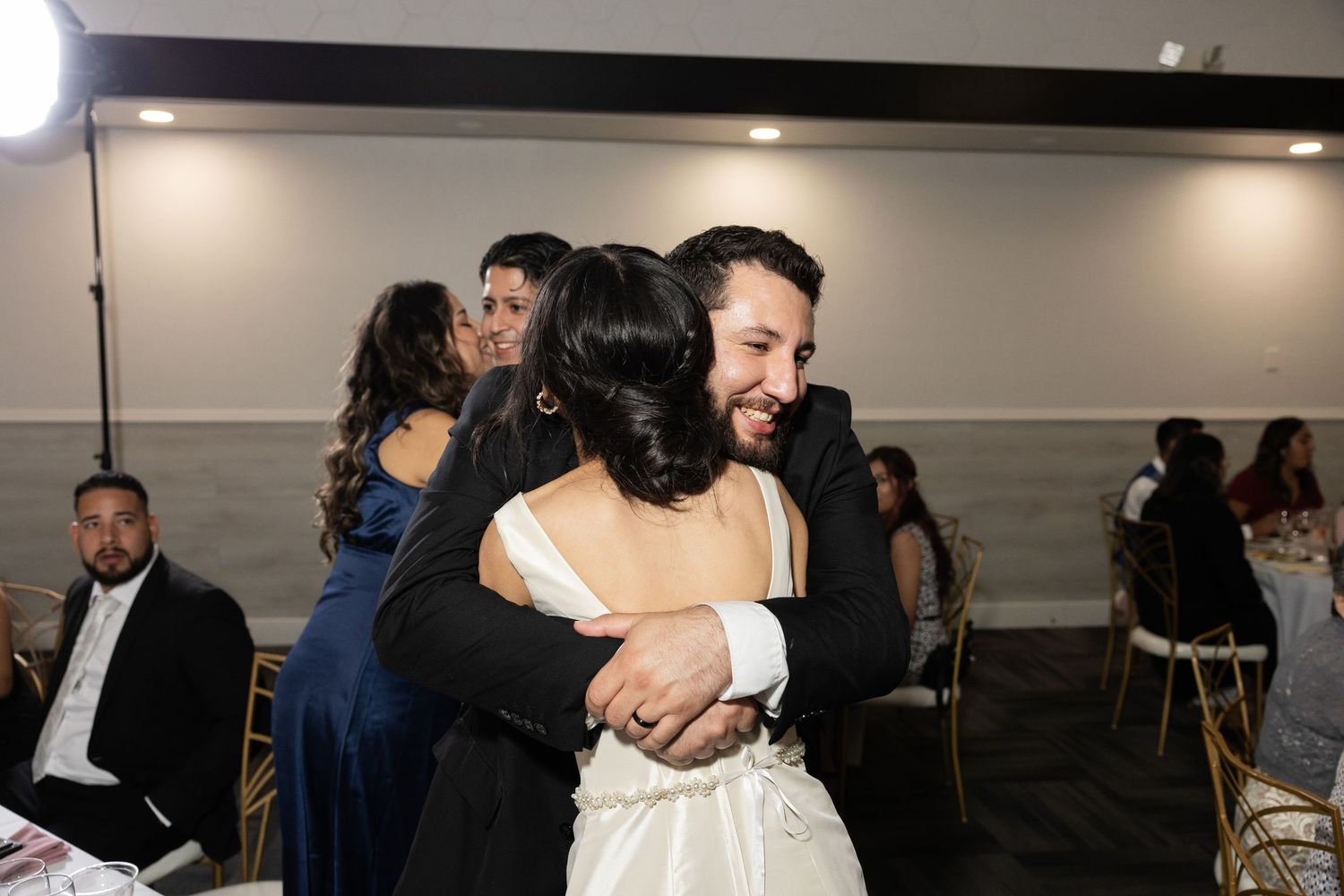 Wedding reception celebration with guests embracing during emotional moment.
