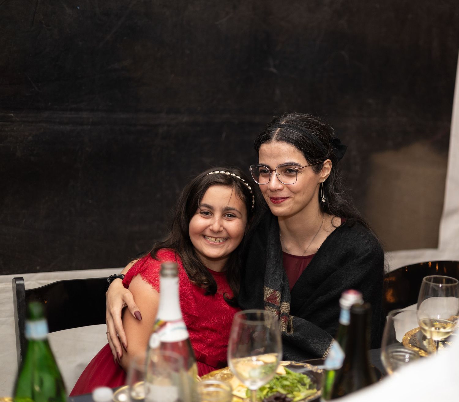 Wedding reception guests enjoying conversation at a rustic venue with wine glasses and decorative greenery.