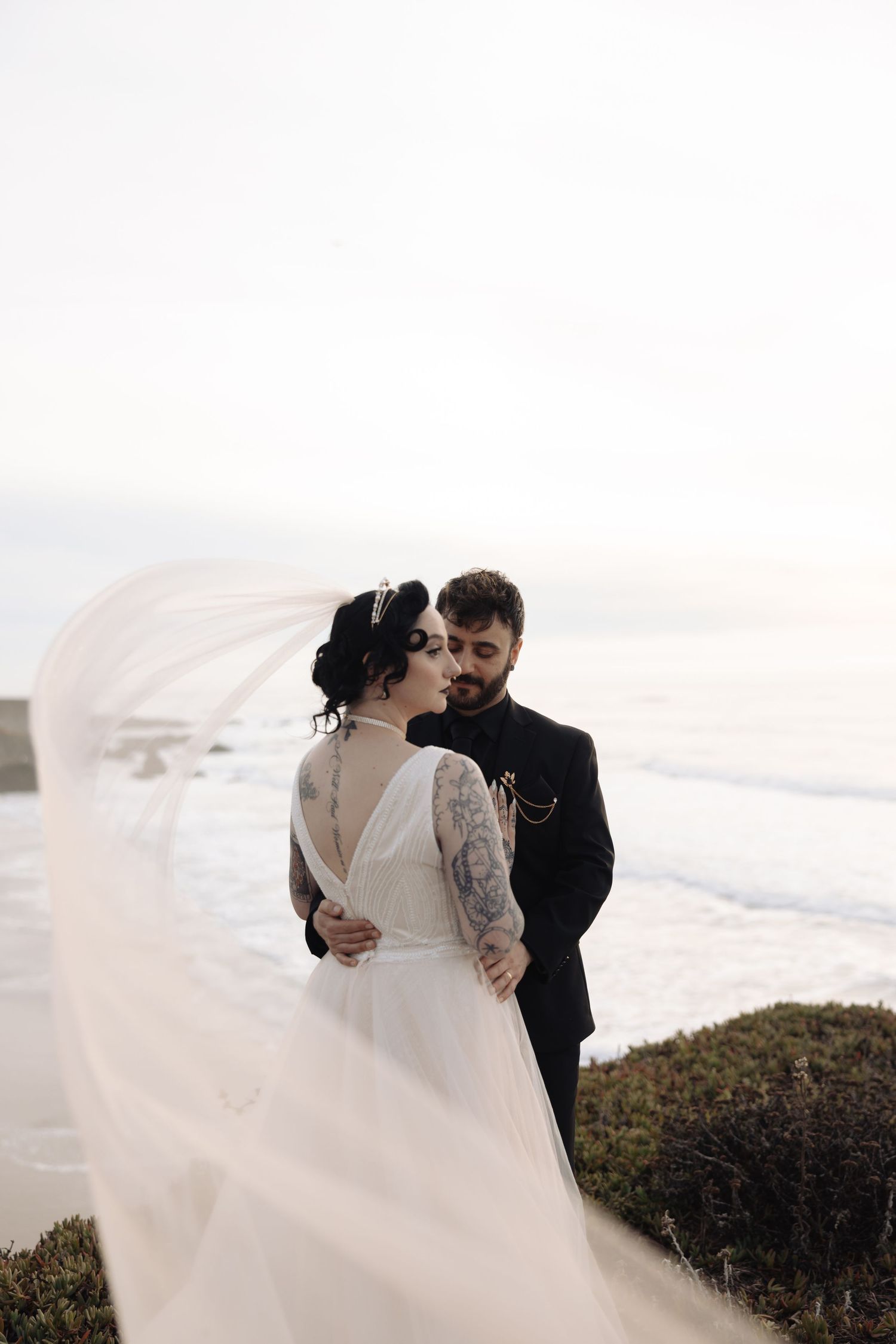 Dramatic wedding photography on coastal cliffs with flowing white dress in the wind.