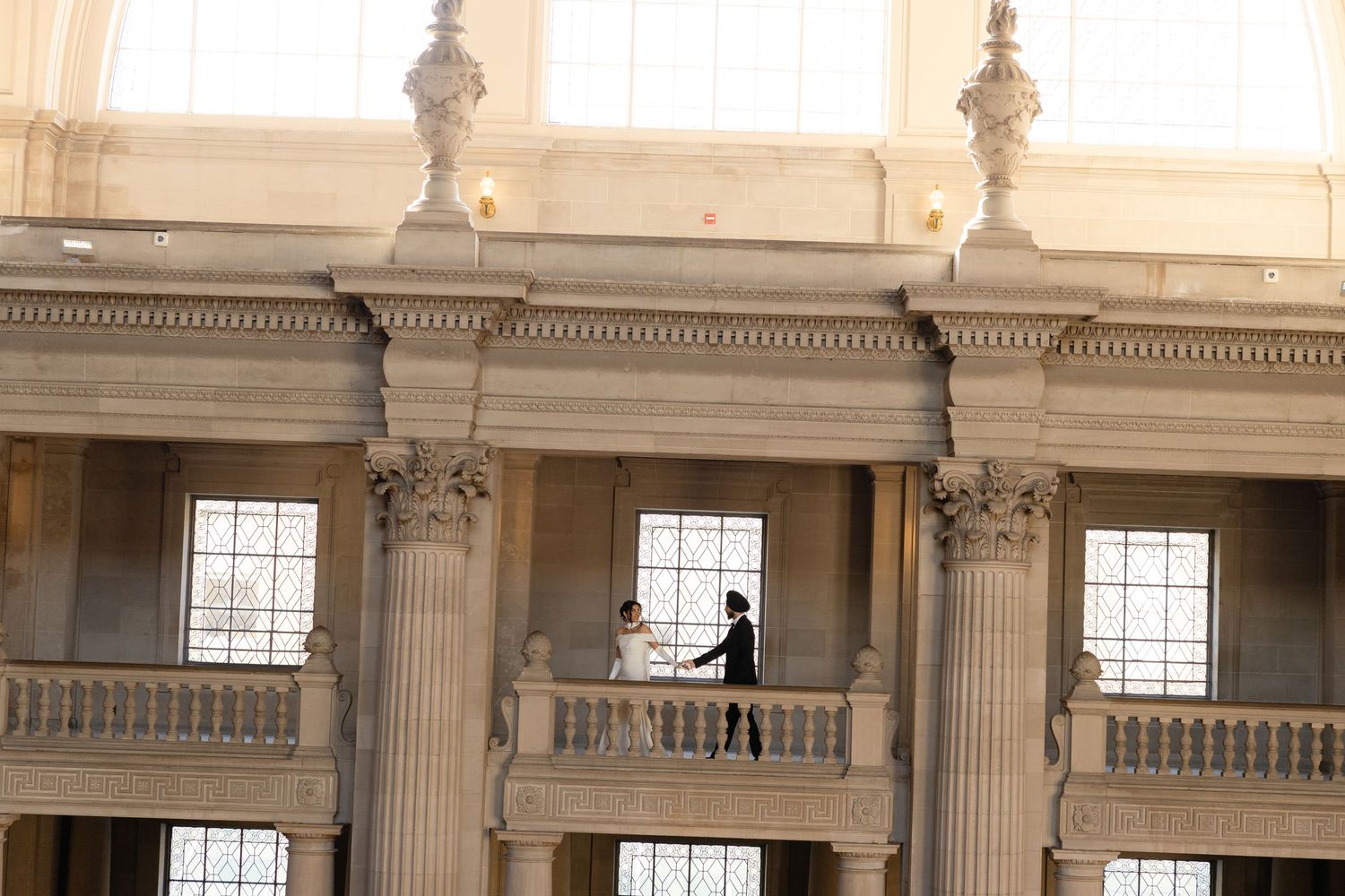 A silhouetted figure stands on an ornate balcony with classical columns and architectural details in warm lighting.