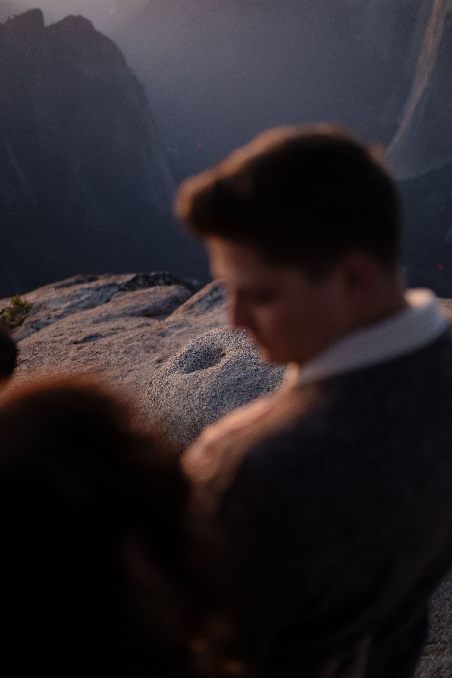 Intimate mountain engagement photo with dramatic cliff backdrop at sunset.