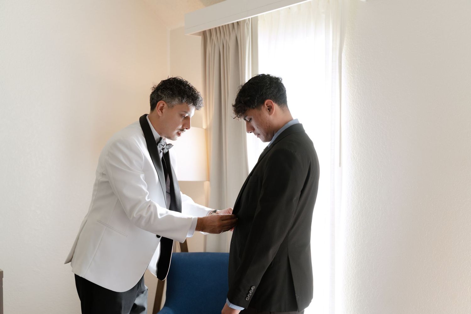 Two people helping each other with formal attire preparations.
