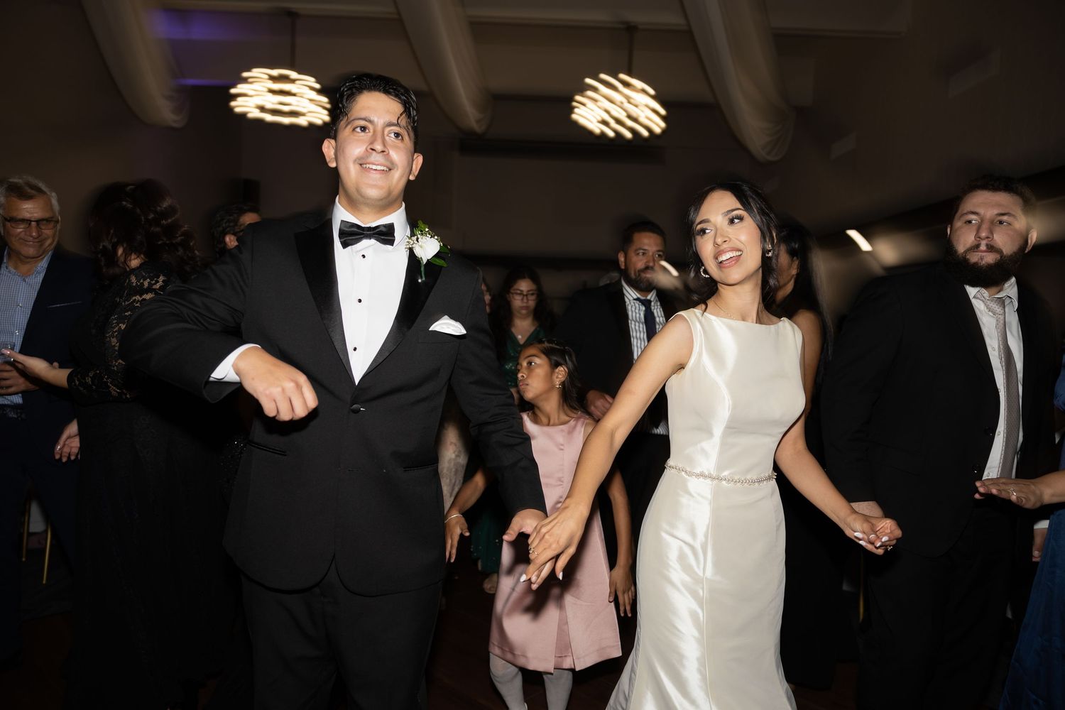 Formal event attendees dancing and celebrating in an indoor venue with ambient lighting.