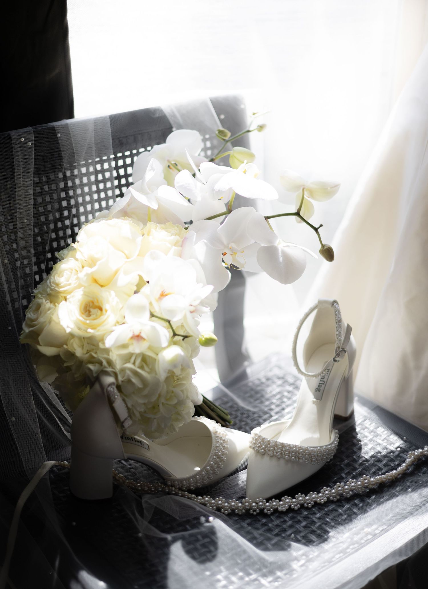 White bridal bouquet and elegant wedding shoes arranged on a dark textured surface.