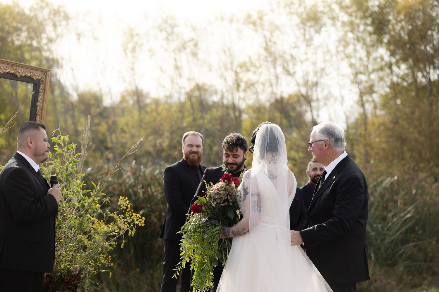 Formal wedding ceremony taking place outdoors with attendants in dark suits.