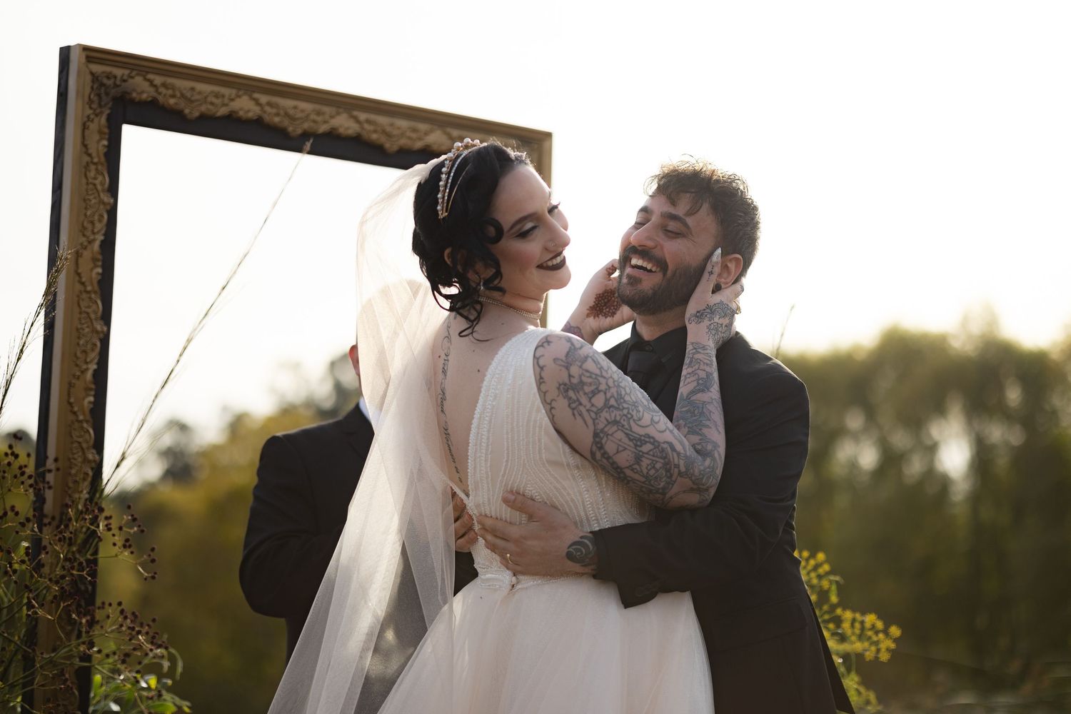 A couple shares a joyful moment under a wooden arch during their outdoor wedding ceremony.