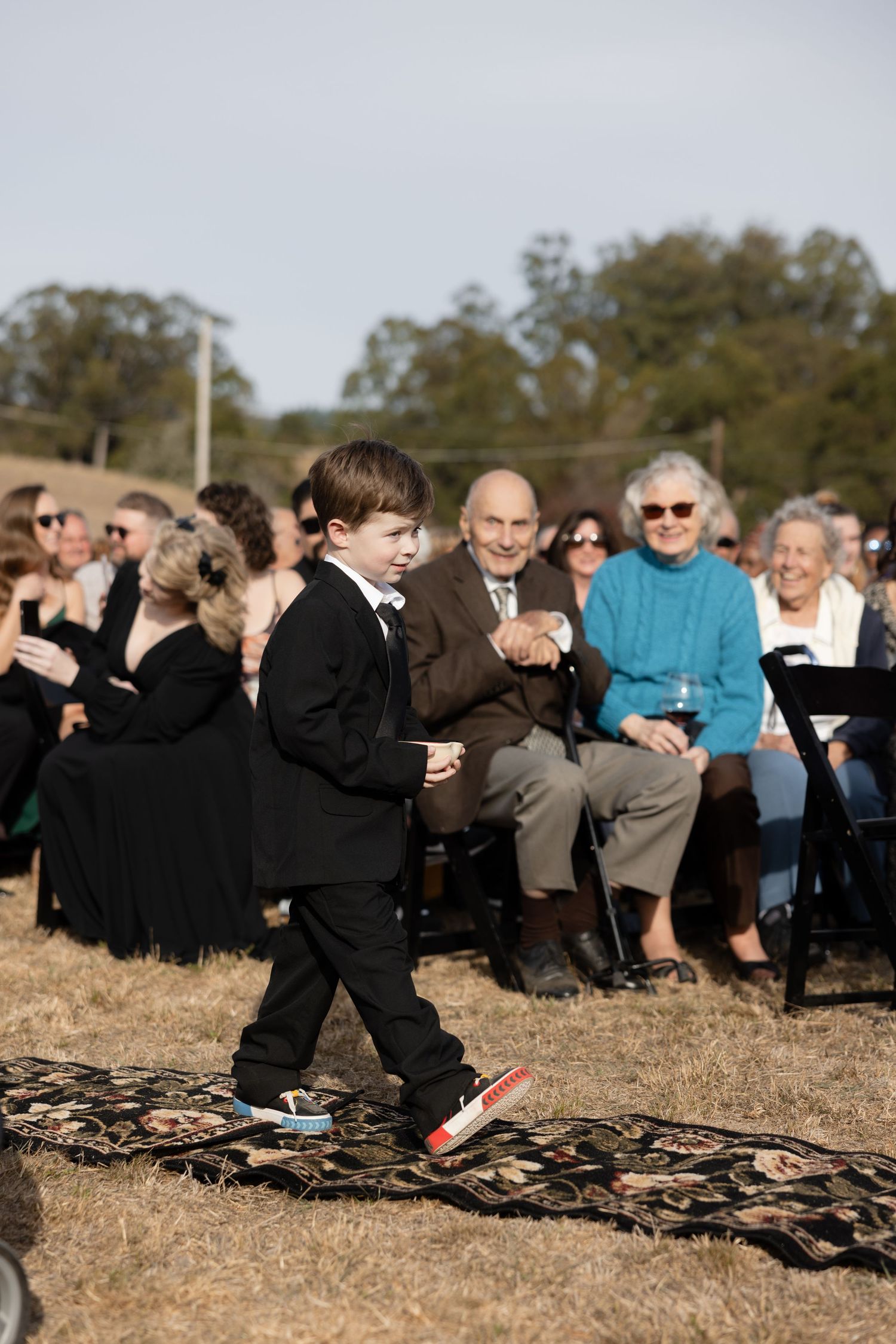 Wedding ceremony guests seated on blankets in an outdoor field setting.