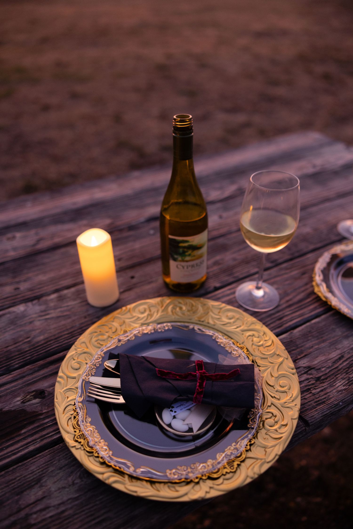 Elegant table setting with gold charger plates and wine glasses on rustic wooden surface.