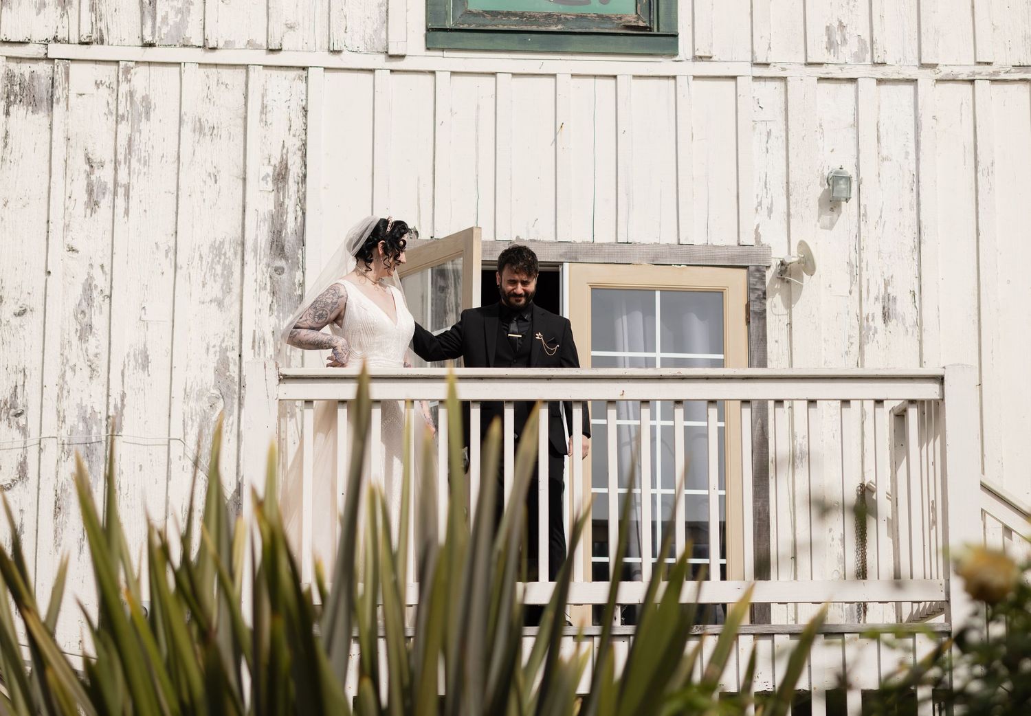 Side view of white barn wedding venue with wooden deck and coastal vegetation.
