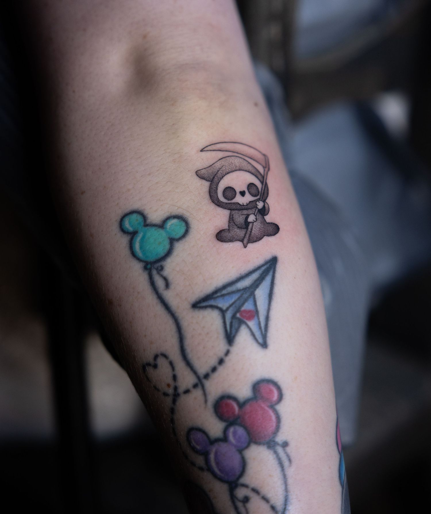 Whimsical tattoo featuring Mickey Mouse balloons, a paper airplane, and a cute cartoon character.